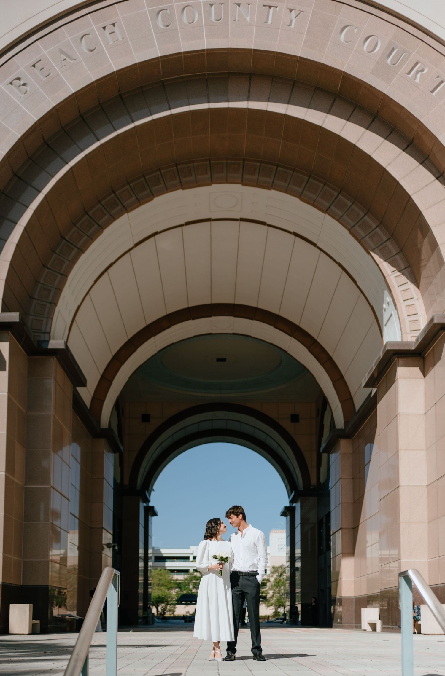 Couple shares romantic moment under grand arched entrance of Palm Beach County Courthouse on their wedding day.