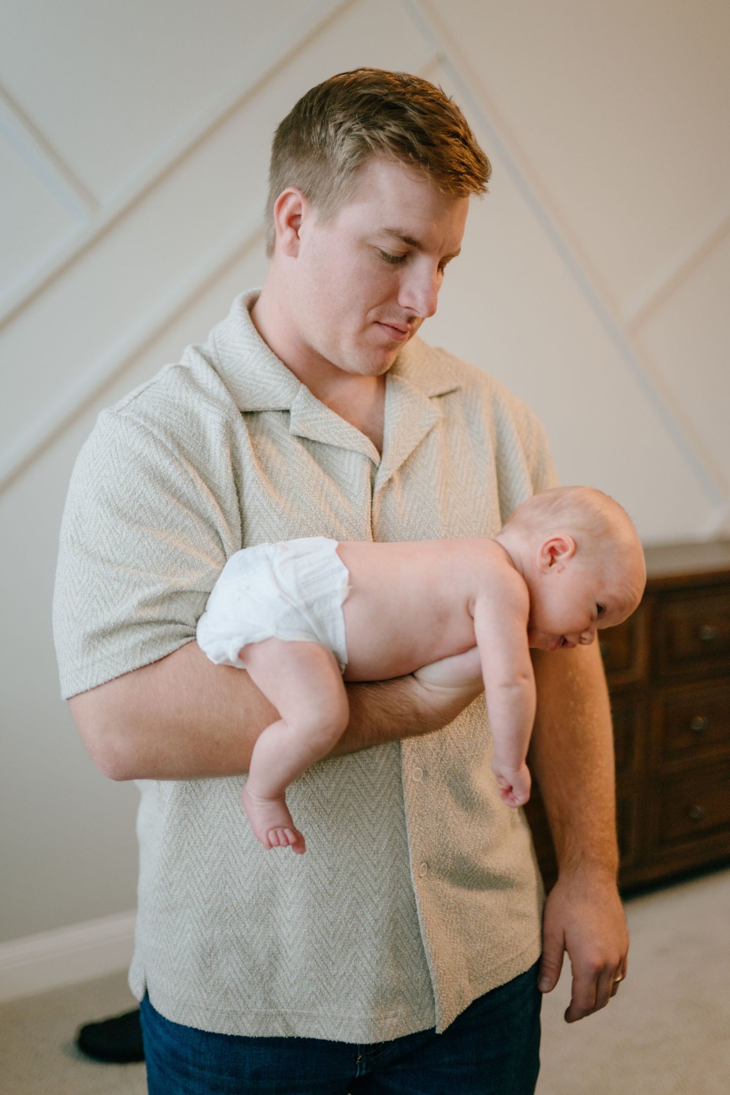 A father in a beige shirt tenderly holding his sleeping newborn baby in his arms.