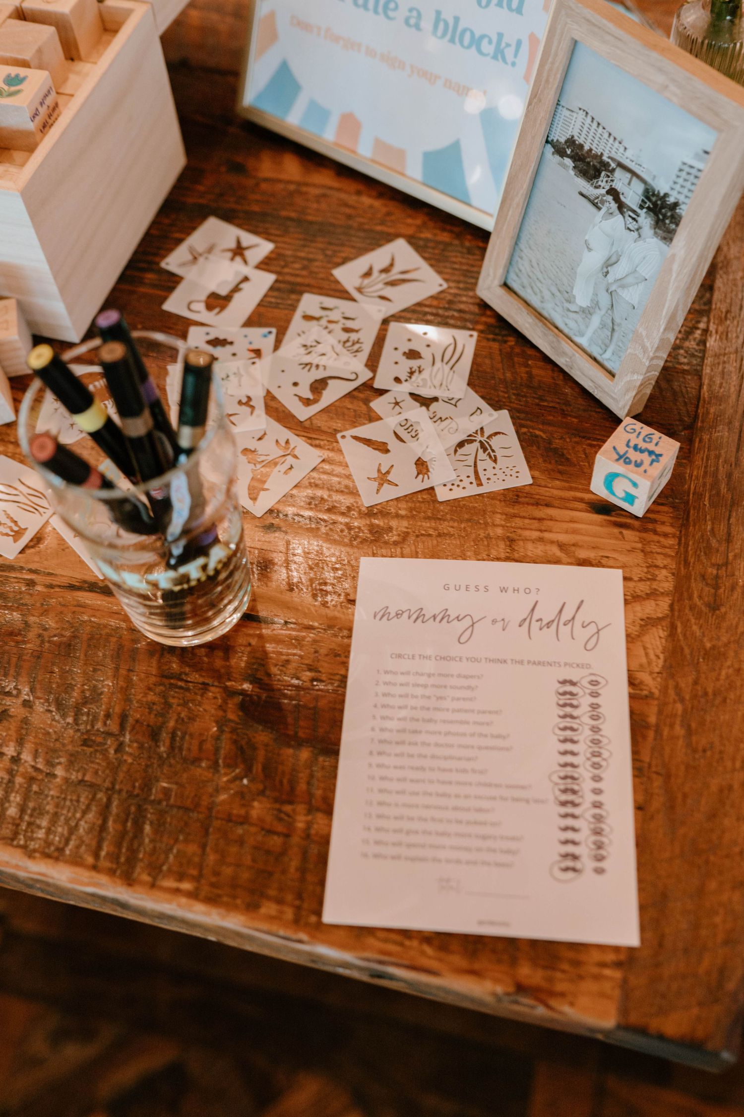 Baby shower activity table with mommy or daddy game sheet, stencils, and decorated wooden blocks craft station.