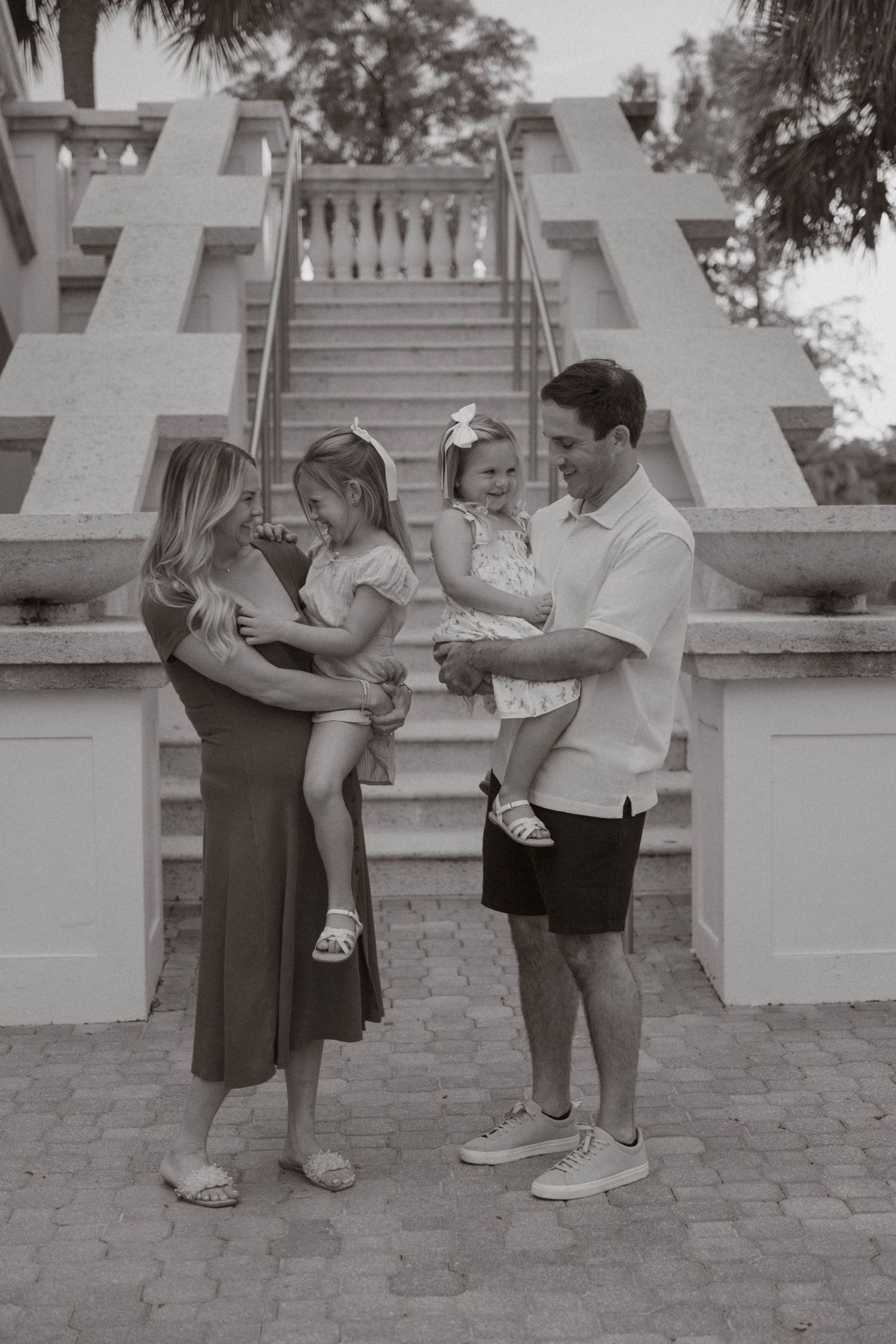 A black and white photo of a family of four with two young girls at an outdoor staircase.