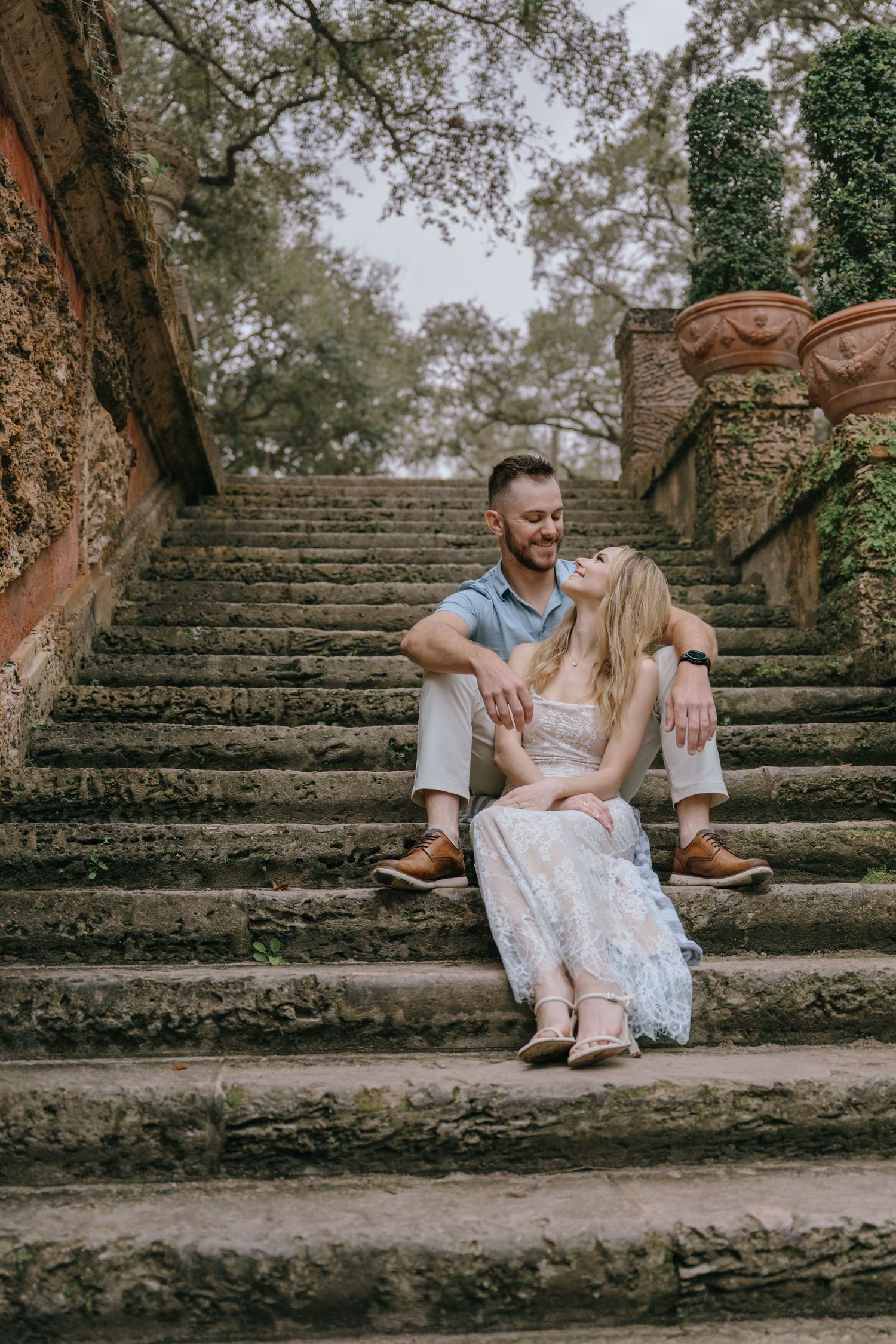 Couple sitting and laughing together on ancient stone steps in a garden.
