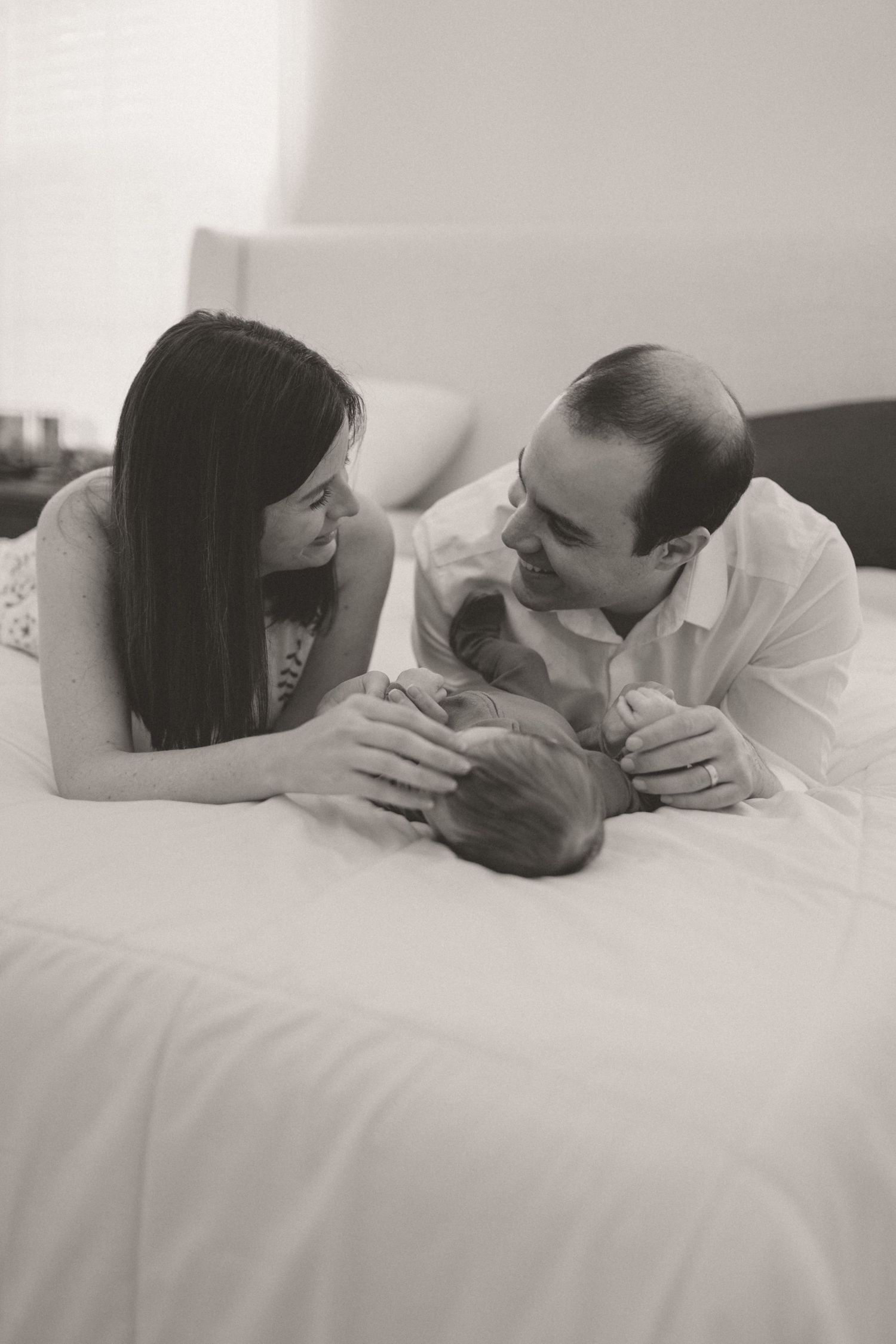 Black and white photo of parents lying on bed gazing at their newborn baby.