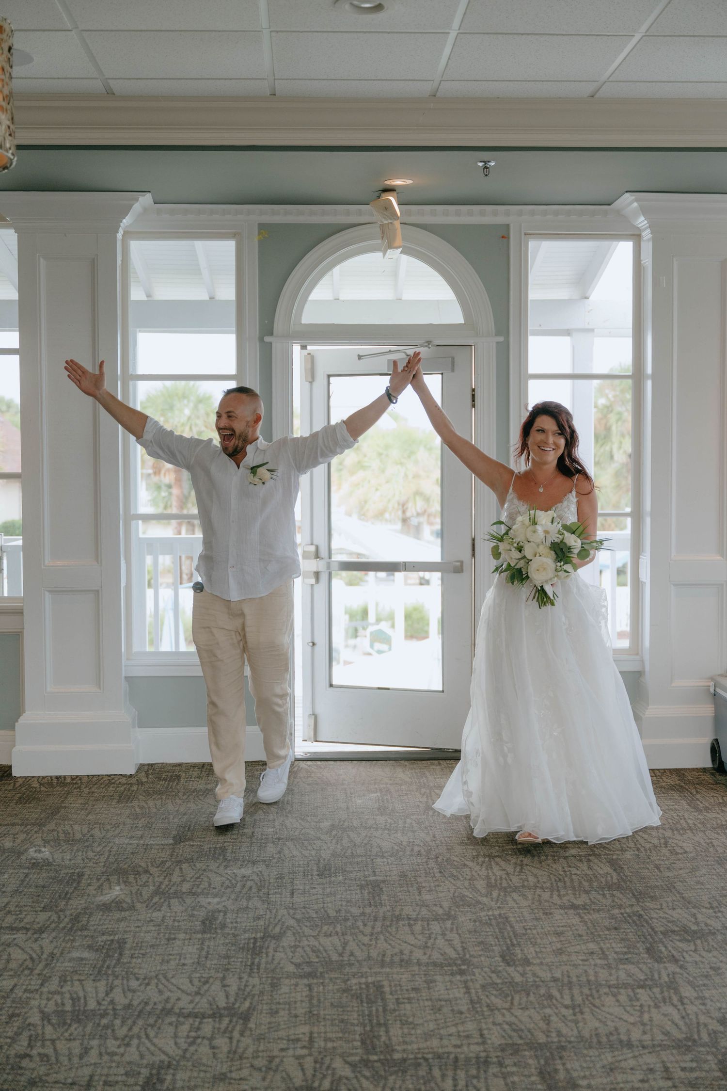 Joyful newlyweds make grand entrance into wedding reception venue with arms raised in celebration.