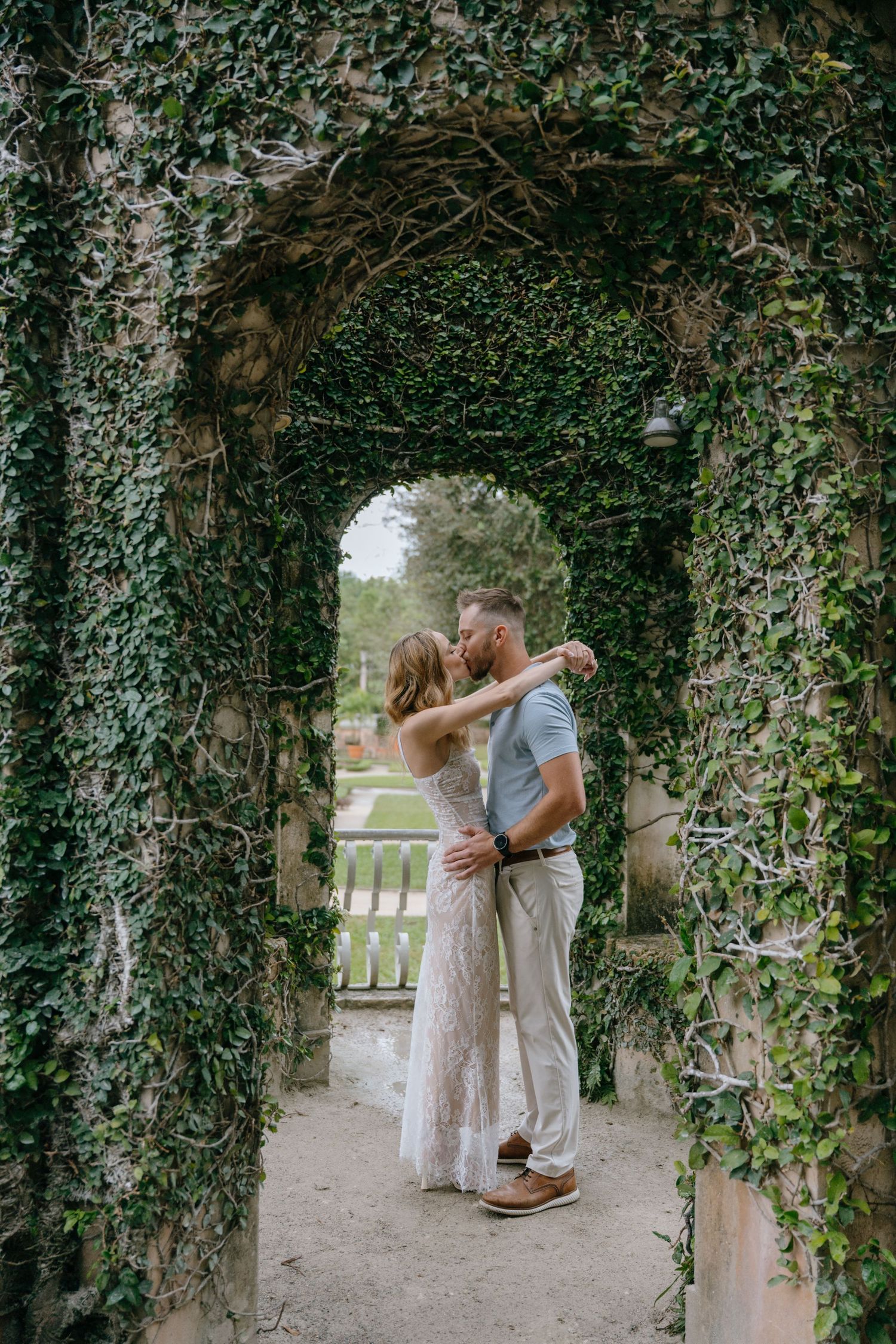 Romantic couple kissing under a lush ivy-covered archway in a garden.