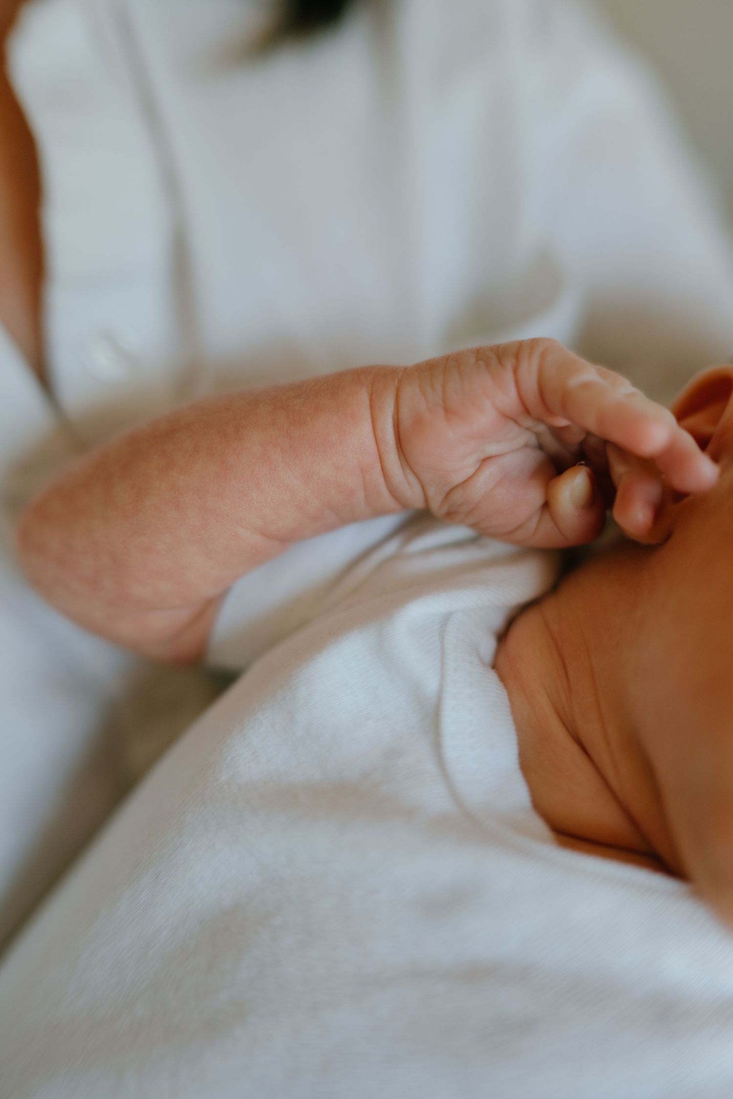 Close-up of a newborn baby's tiny wrinkled hand resting on a white blanket.