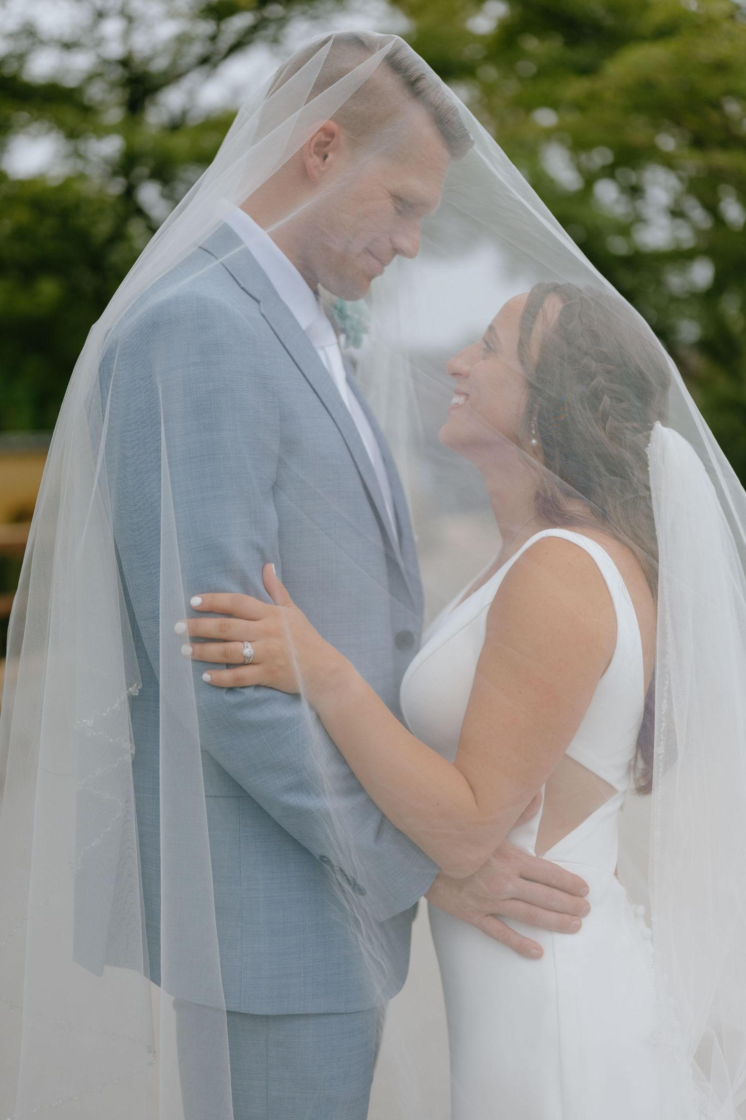 Bride and groom share an intimate moment under a flowing white veil on their wedding day.