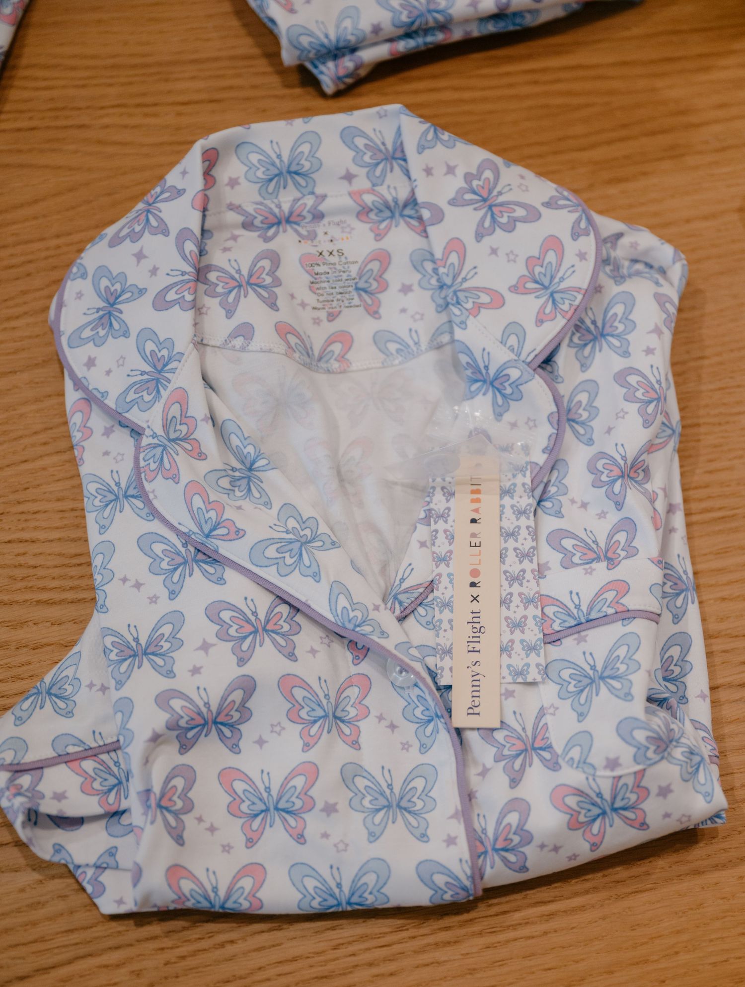 Folded white butterfly print pajama set with Pennys Flight tag on wooden surface.