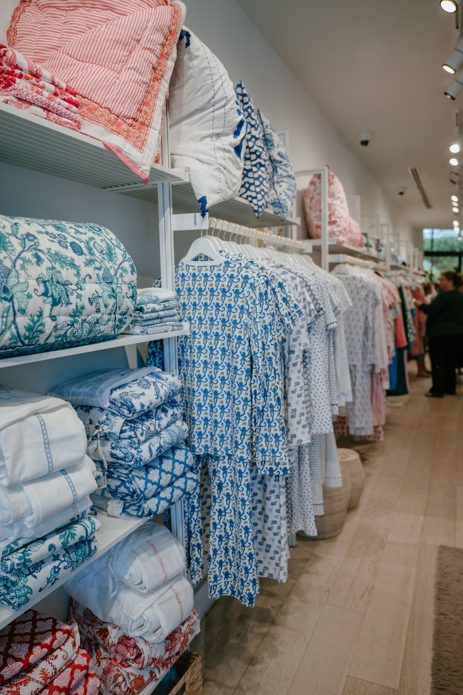 Retail store shelves displaying folded blue and white block print quilts and hanging patterned dresses.
