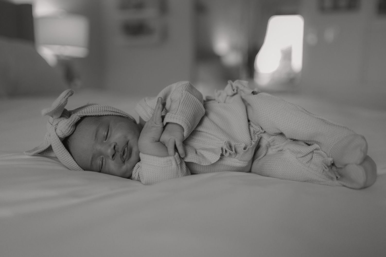 Black and white photo of a peaceful sleeping newborn baby on a white bed.