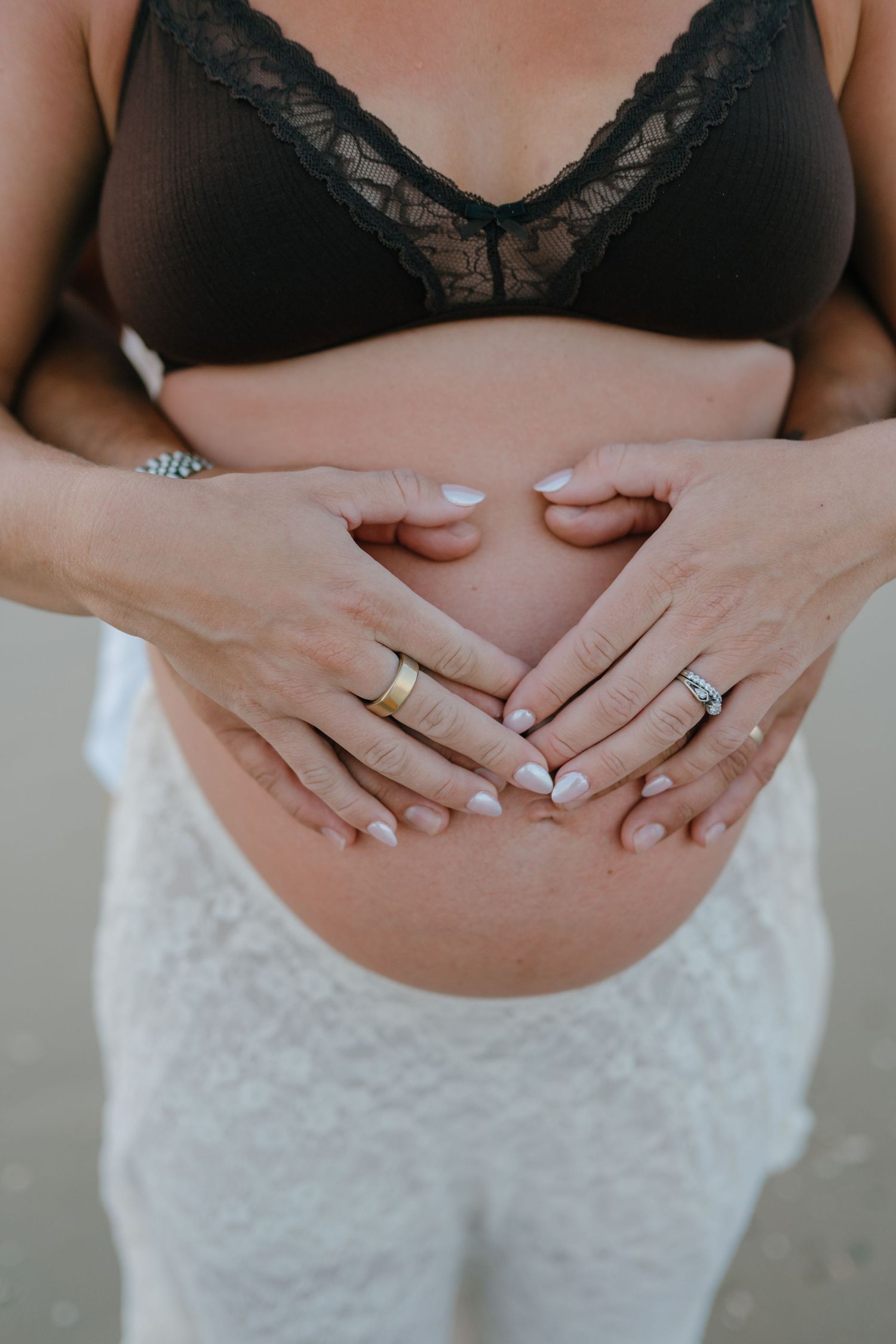 Close-up of couple's hands forming heart shape on pregnant woman's bare belly.