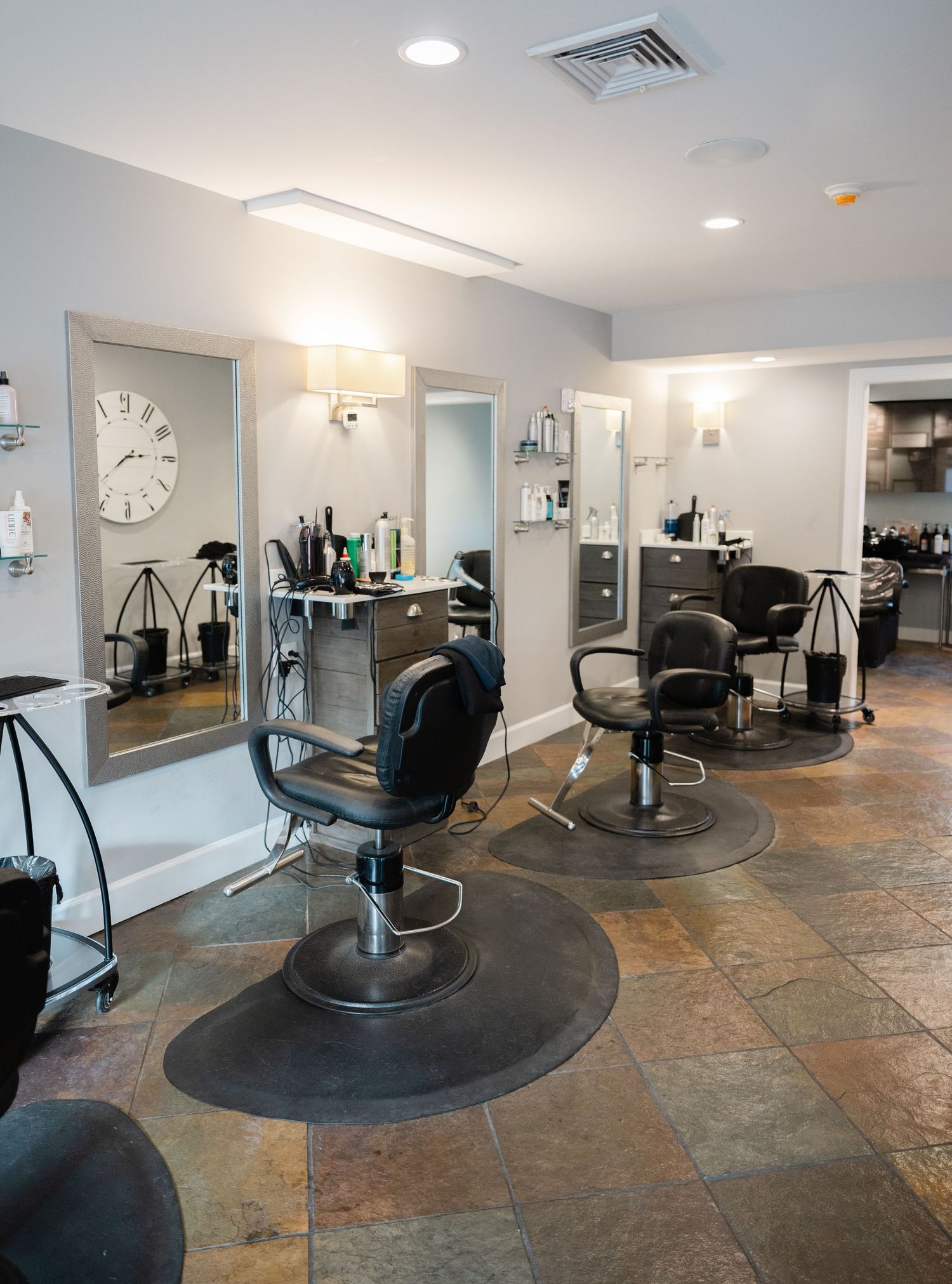 Modern hair salon interior with black styling chairs, large mirrors, and slate tile flooring in a clean neutral space.