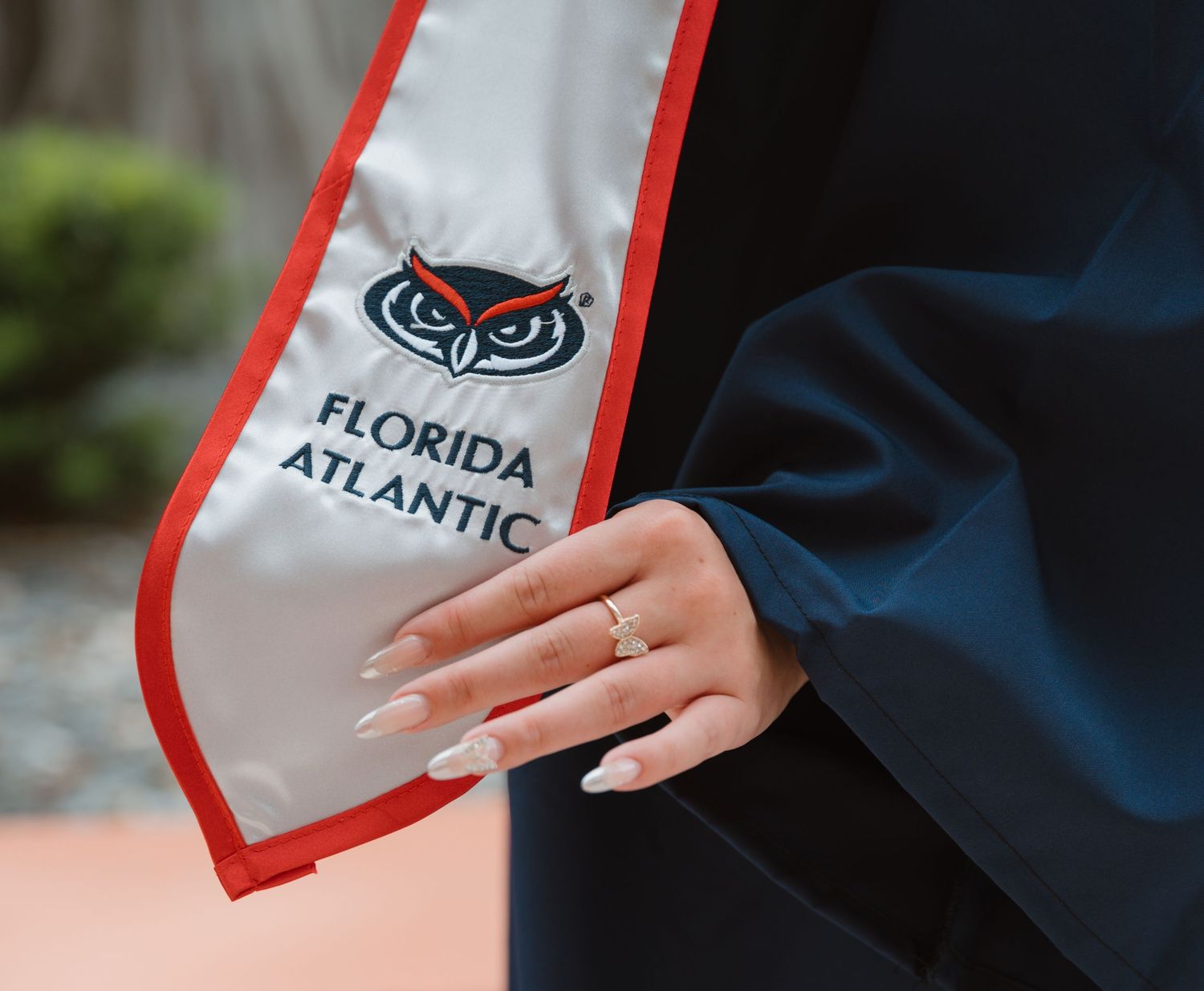 Close-up of Florida Atlantic University graduation stole with owl logo and graduate's manicured hand.