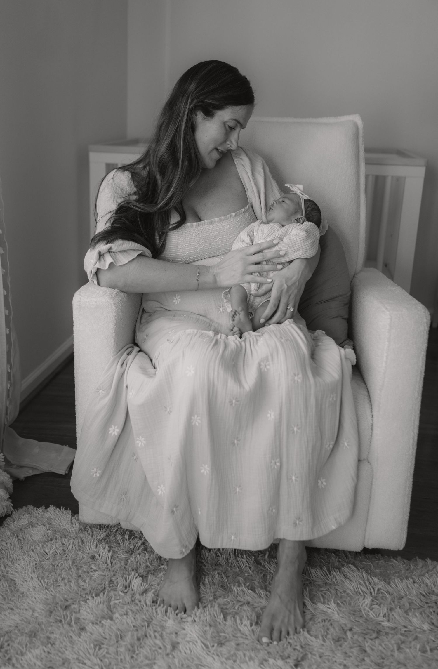 Black and white photo of mother sitting in nursery chair cradling newborn baby.