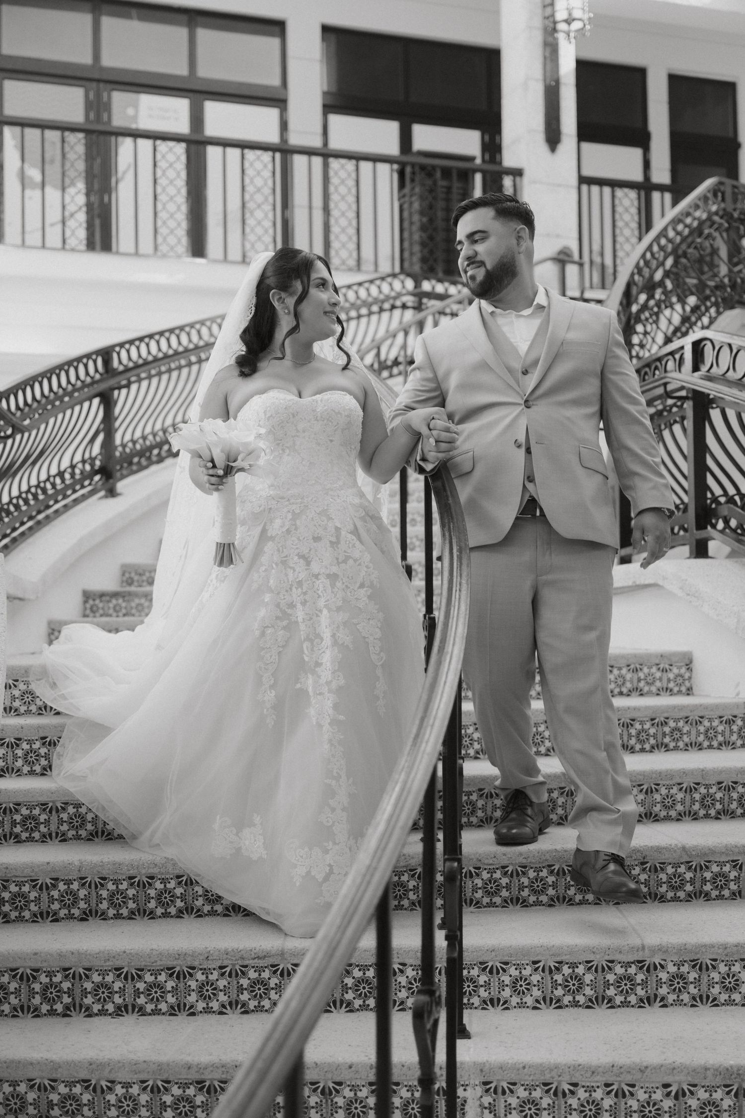 Black and white photo of bride and groom posing on ornate tiled staircase at wedding venue.