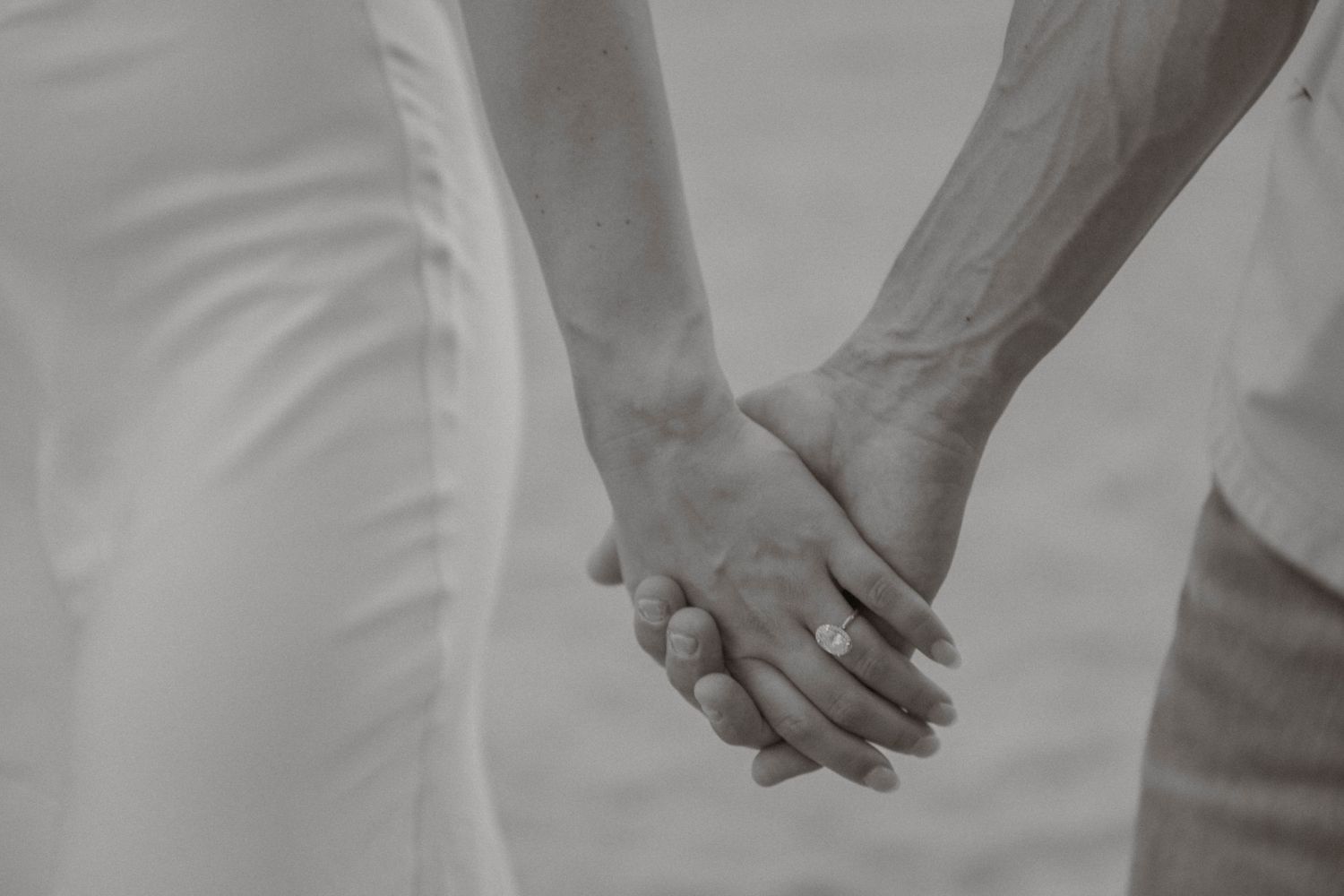 Black and white close-up of an engaged couple holding hands, diamond ring visible on woman's finger.