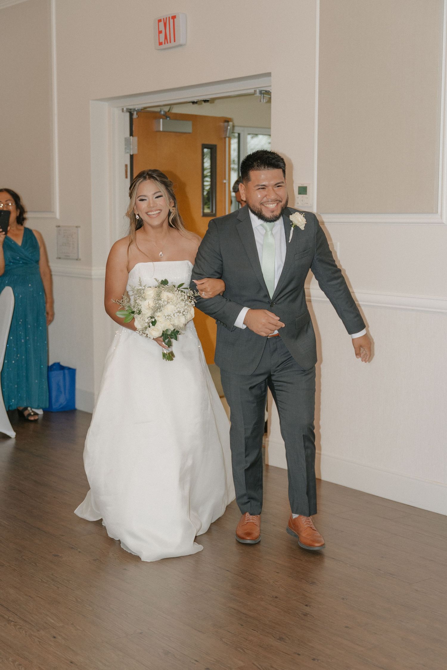 Smiling bride and groom make grand entrance at wedding reception, bride holding white floral bouquet.