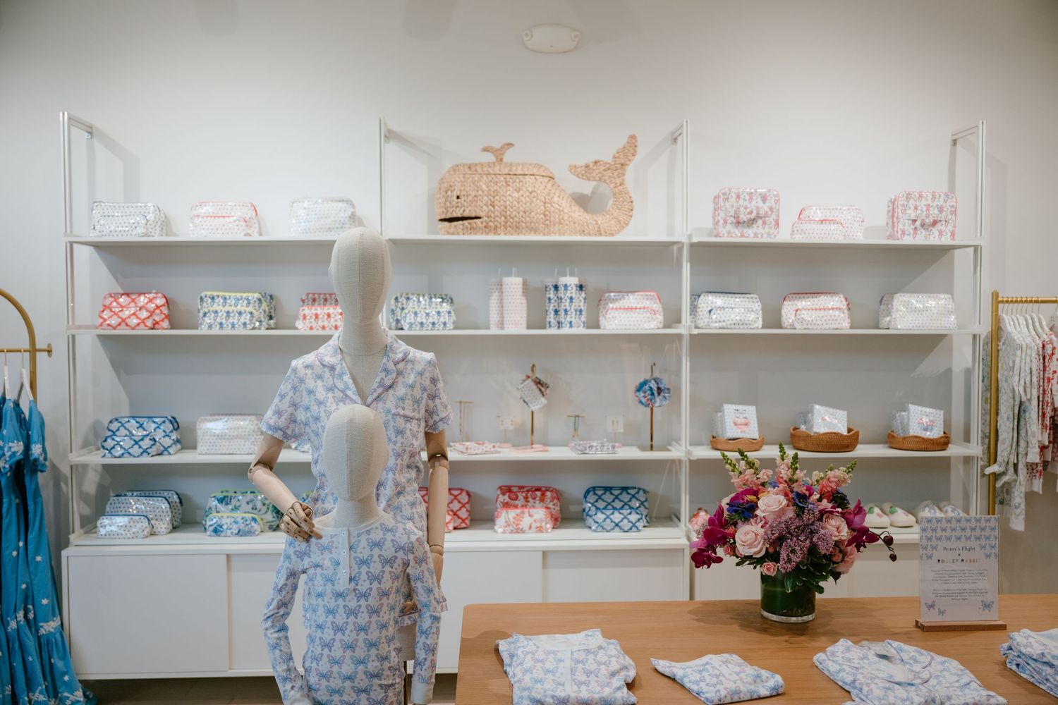 Bright boutique interior with mannequin in blue print dress, white shelves, and fresh flower arrangement.