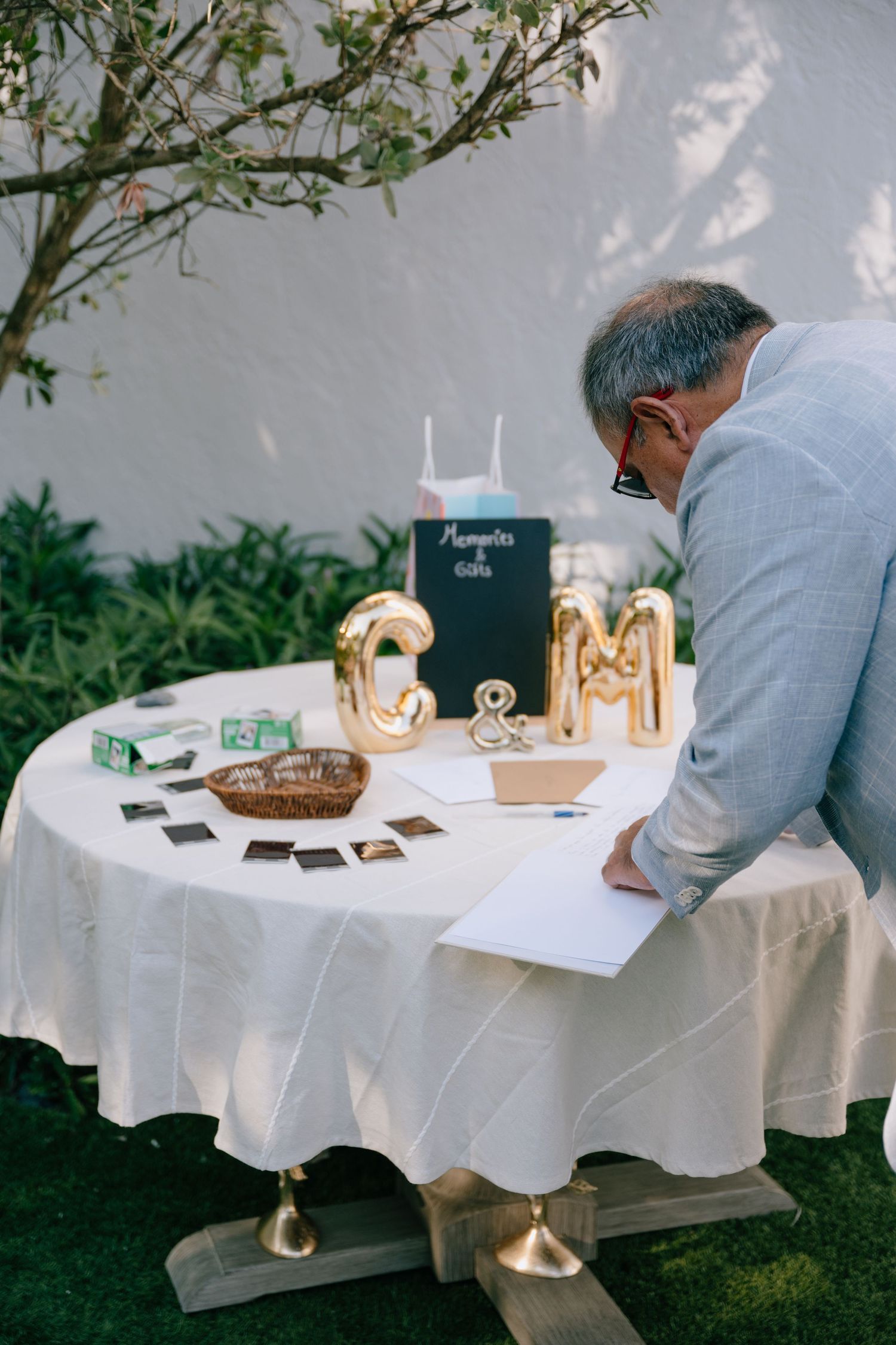 Guest signing the wedding guestbook at a decorated outdoor table with gold GM balloon letters.