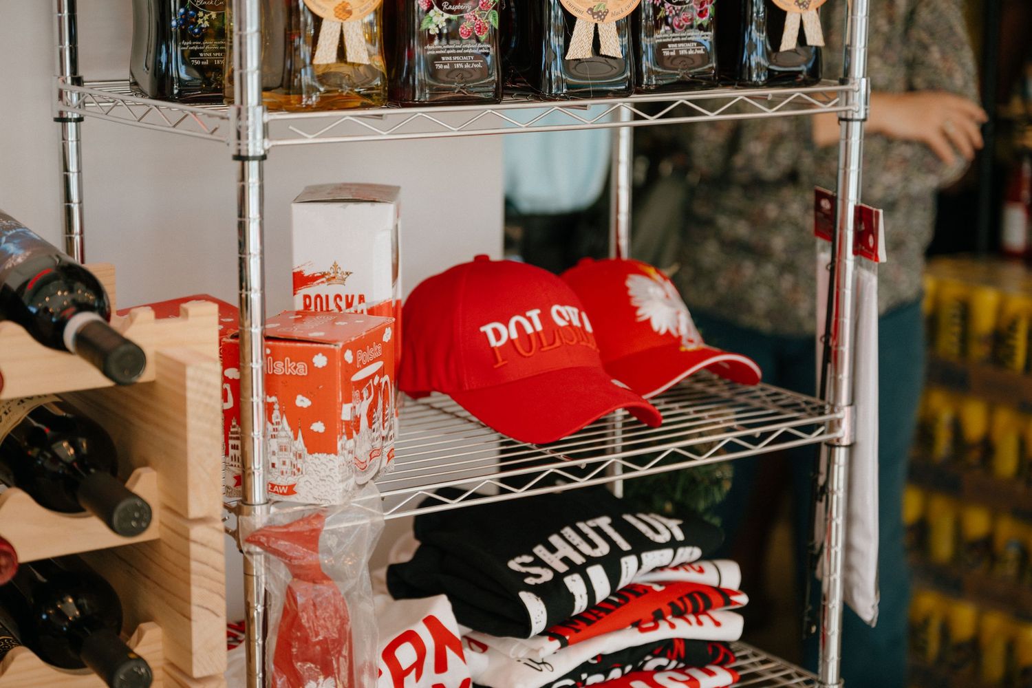 Red Polish Deli branded caps, merchandise cups, and folded t-shirts displayed on a chrome retail shelf.