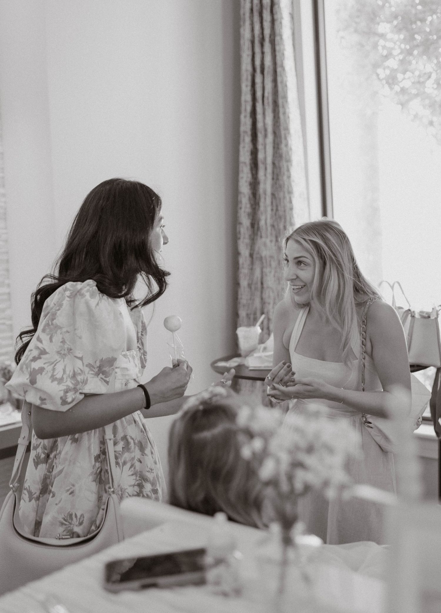 Two women laughing and chatting in black and white photo at a social gathering.