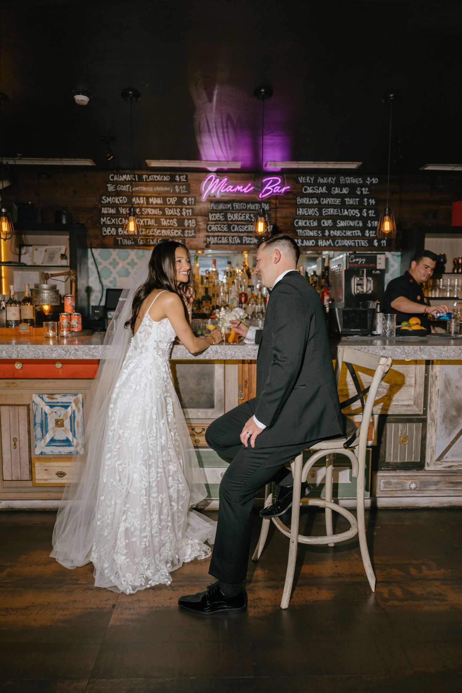 Bride and groom sharing an intimate moment at a dimly lit bar with a glowing Miami Bar neon sign.