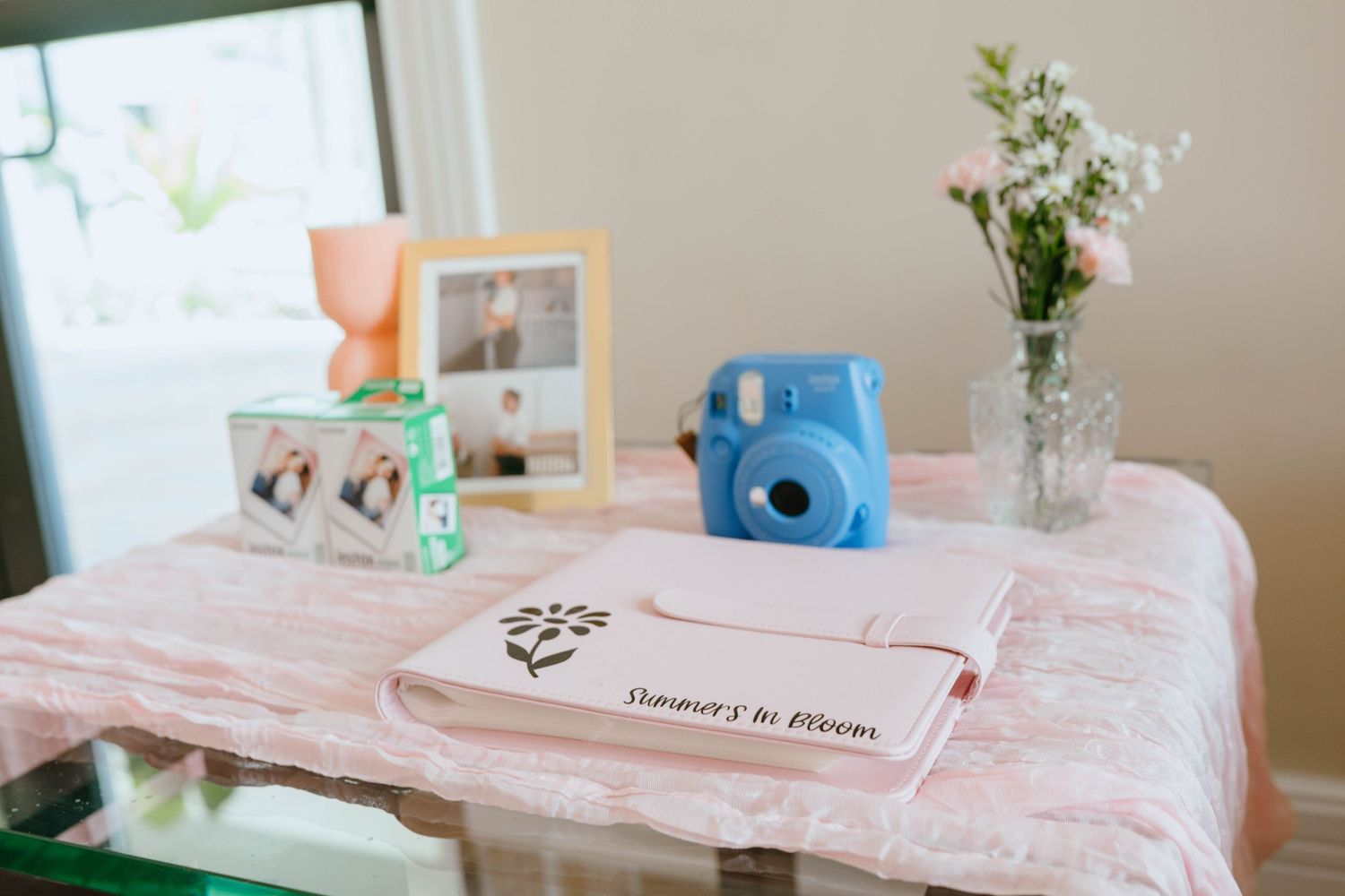 Baby shower guest book table with blue Instax camera, photo frames, and fresh flowers.