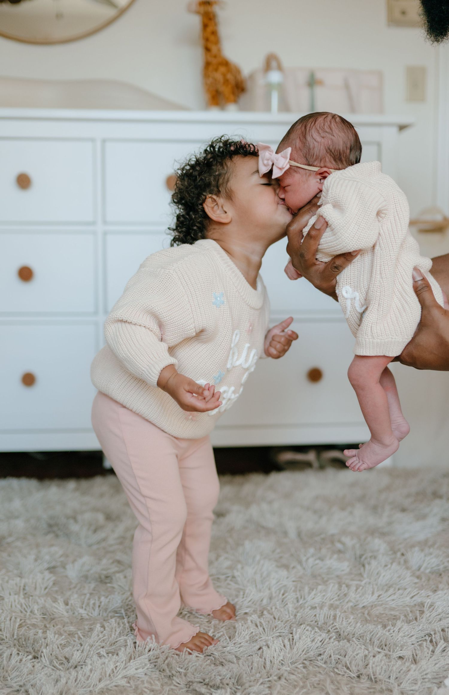 Toddler girl giving a sweet kiss to her newborn baby sister in a nursery.