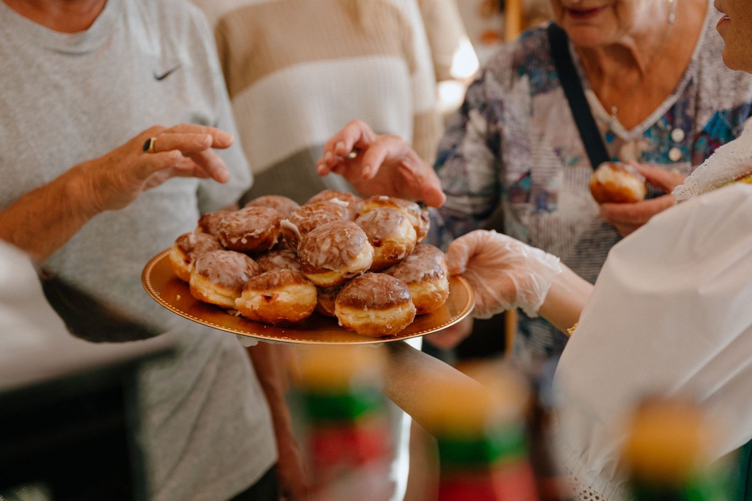 Elderly women sharing a plate of glazed Polish paczki donuts at a social gathering or store event.