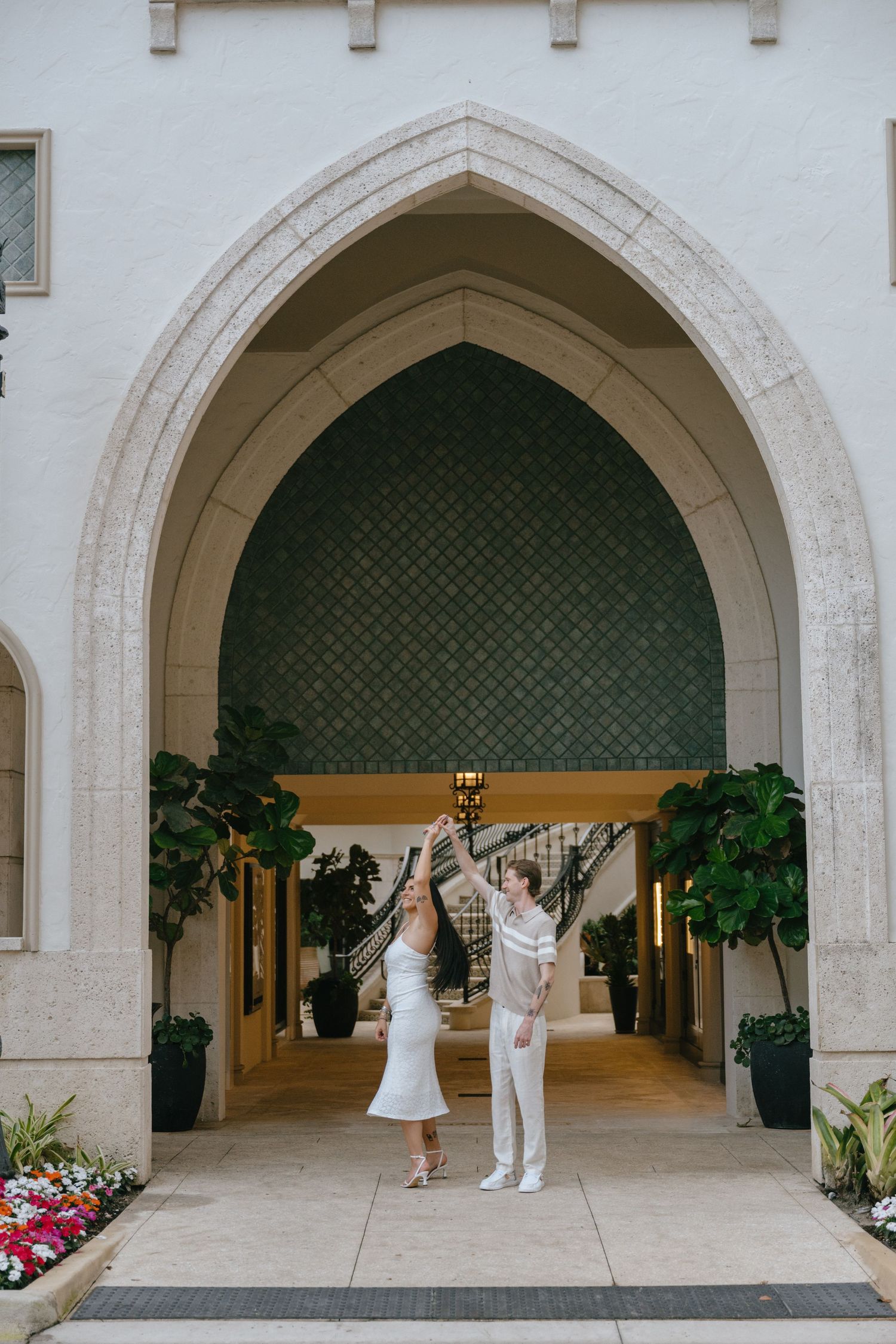 Joyful couple dancing and raising hands under an elegant Gothic arch entrance of a luxury Palm Beach building.