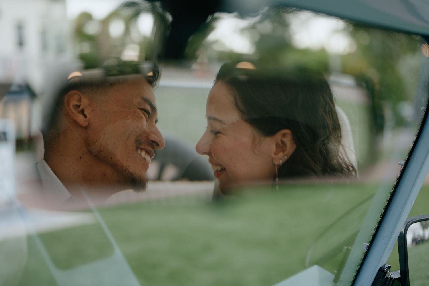 Happy newlywed couple smiling at each other through the window of a vintage light blue car.
