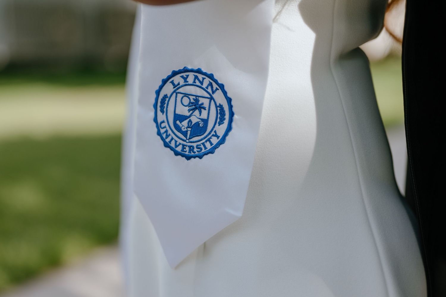 Close-up of white graduation stole featuring Lynn University blue seal emblem.