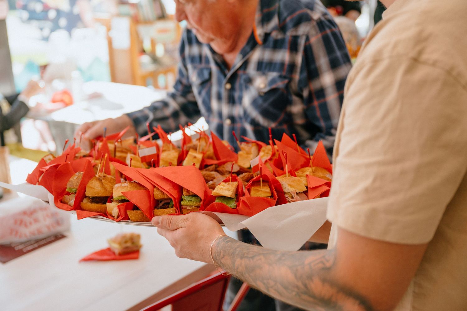 Person holding a tray of mini sandwiches wrapped in red paper at a Polish deli grand opening event.
