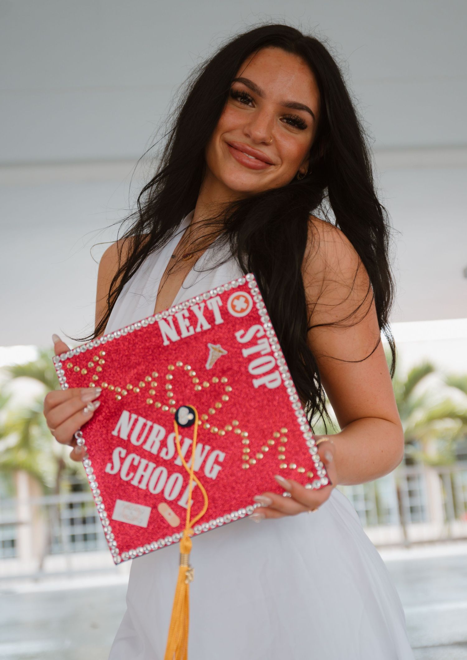 Smiling graduate holds decorated red cap reading Next Stop Nursing School at FAU graduation.