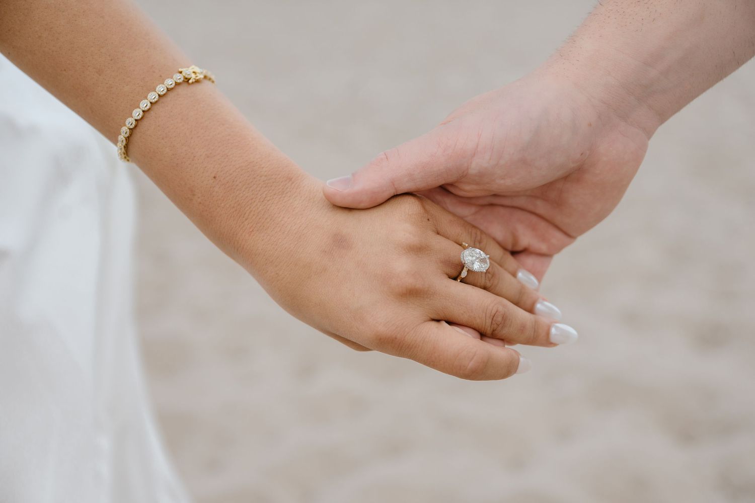 Close-up of couple holding hands showing large oval diamond engagement ring and gold tennis bracelet.