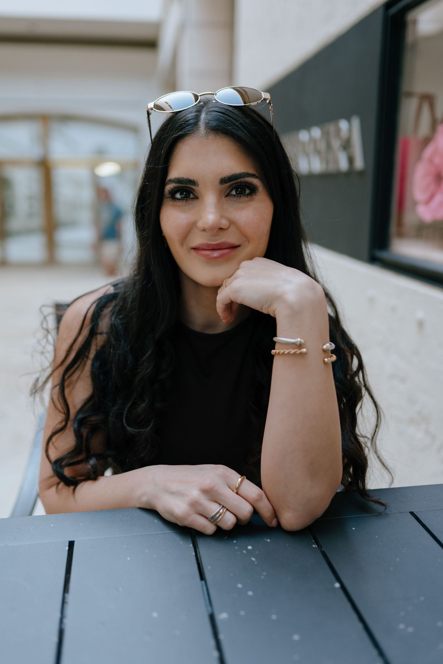 Brunette woman in black top sitting at dark table in shopping mall cafe.
