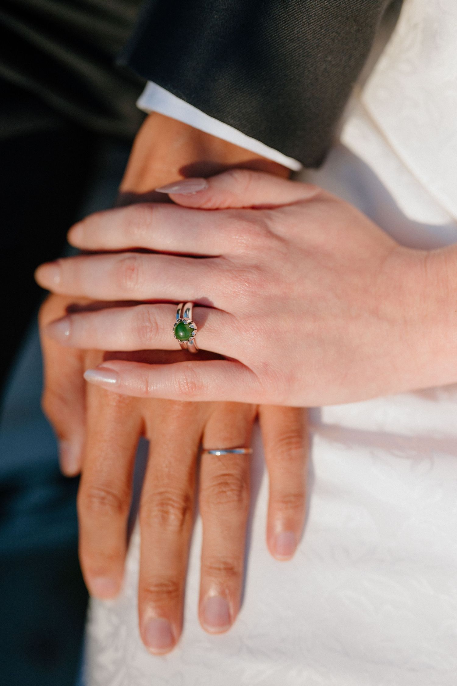 Close-up of bride and grooms hands showing a unique green emerald engagement ring and silver wedding band.