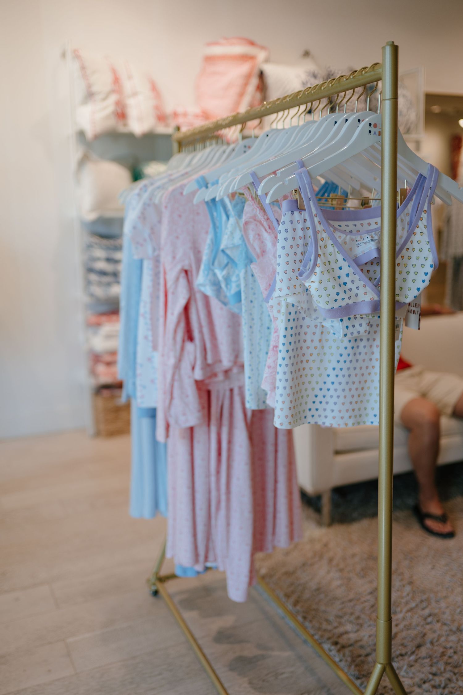 Gold clothing rack displaying pastel pink and blue childrens garments in a boutique shop.