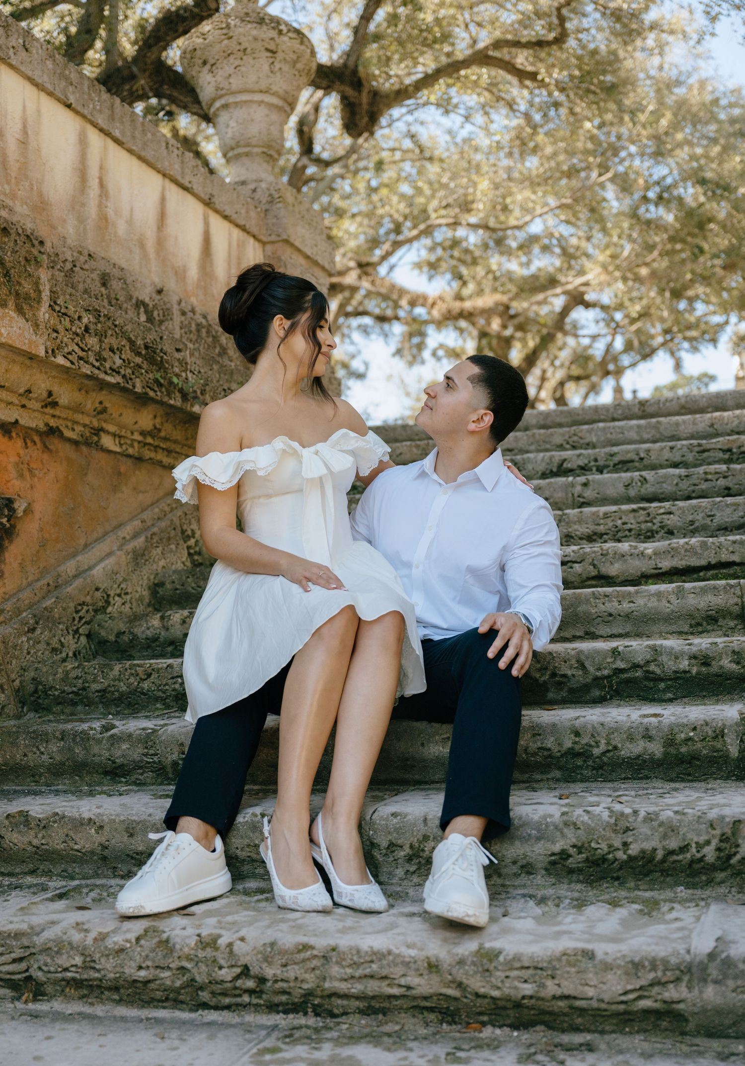 Couple sitting together on ornate stone steps at historic estate, gazing lovingly at each other.