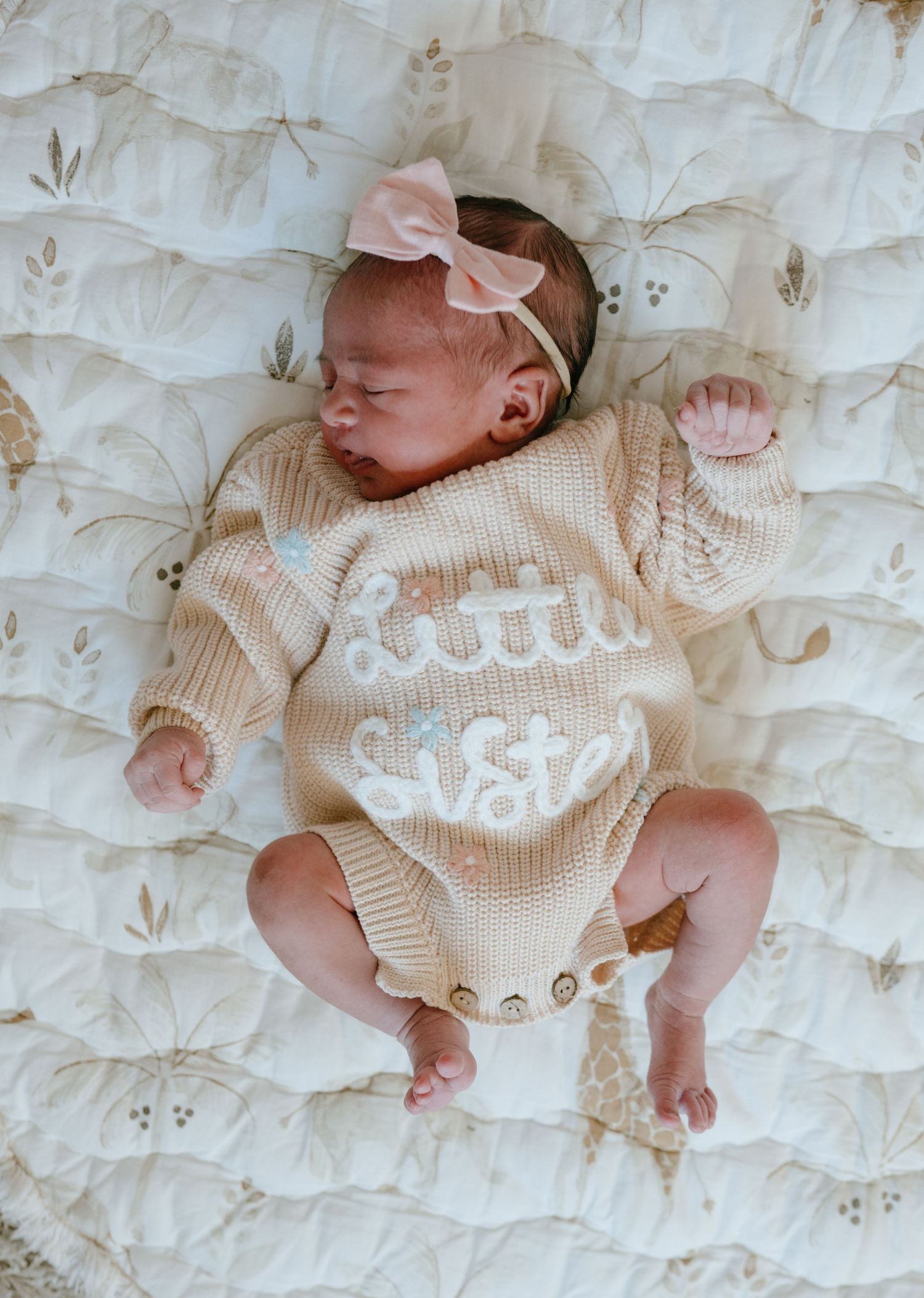 Newborn baby in a knit little sister romper with pink bow headband sleeping.