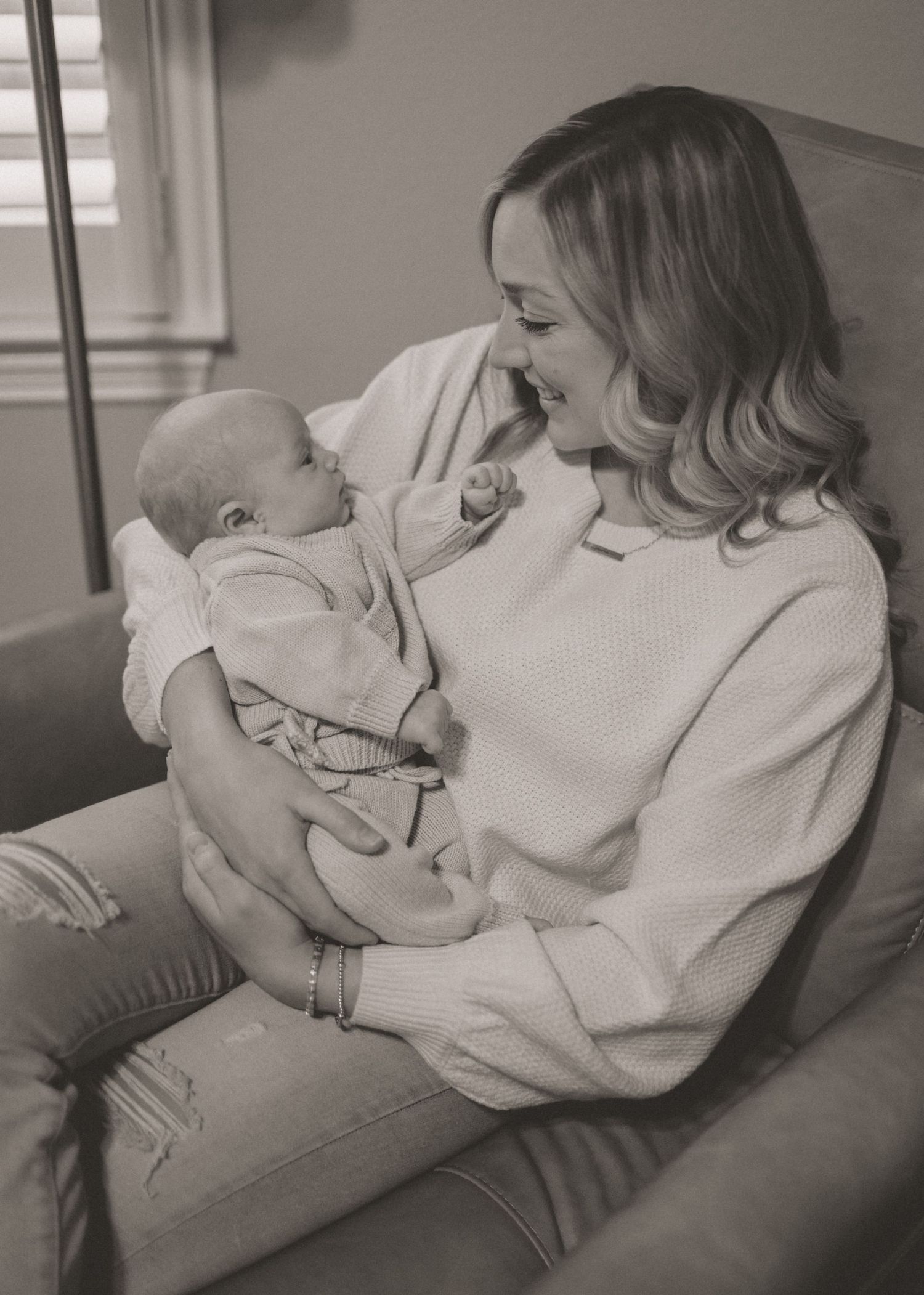 Black and white photo of a smiling mother holding her newborn baby in a cozy chair.