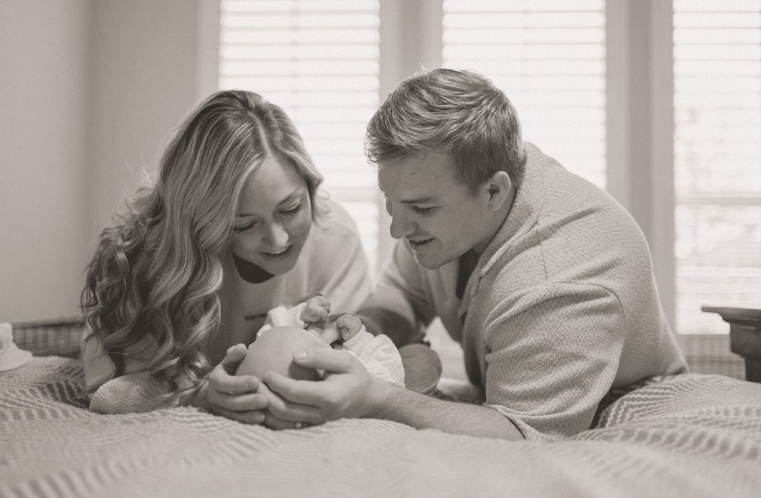 Black and white photo of new parents smiling at their newborn baby lying on a bed.