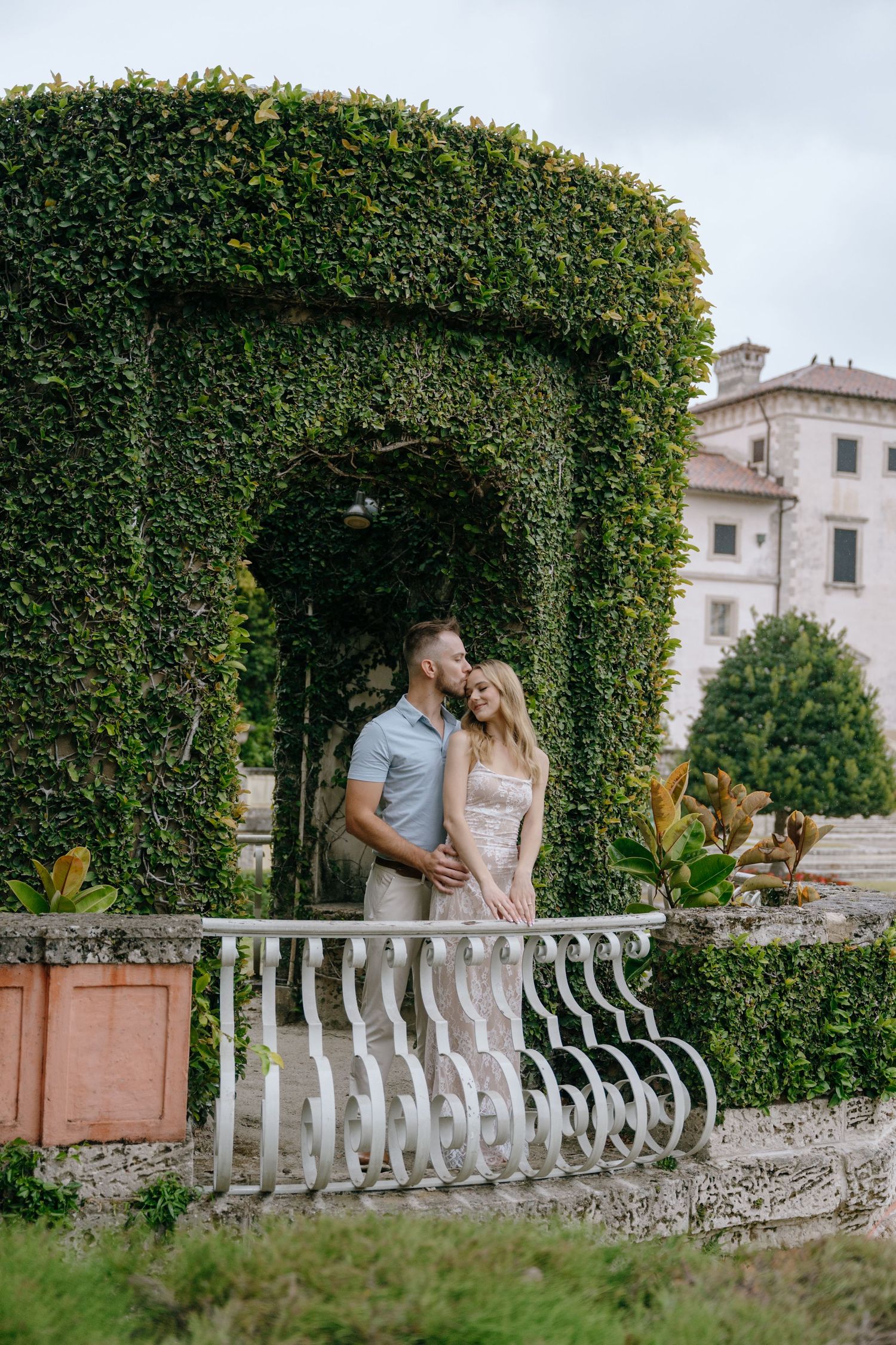Couple embracing under a green hedge archway at a historic estate garden.