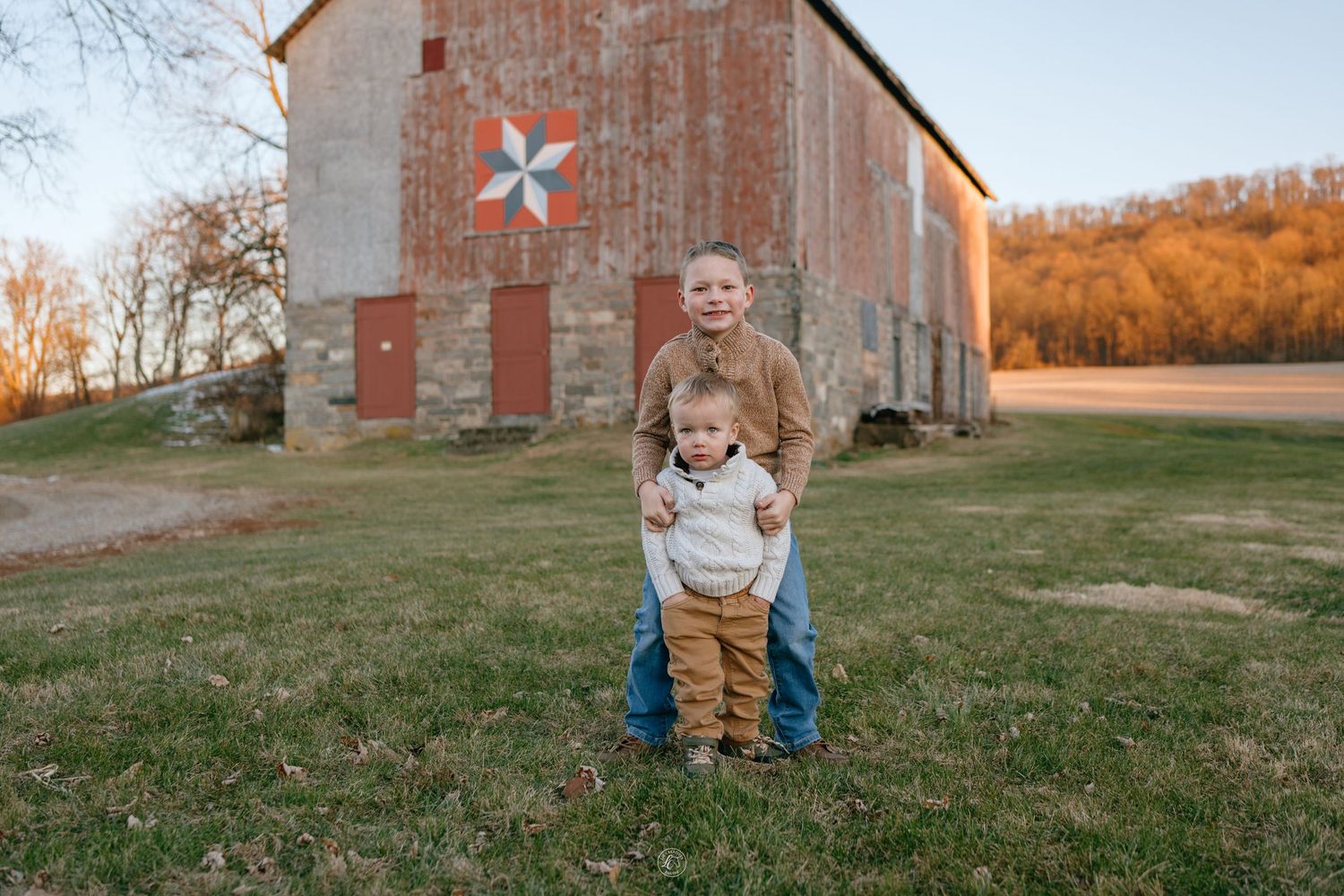 Two young brothers standing together in front of a rustic barn during a fall family photo session.