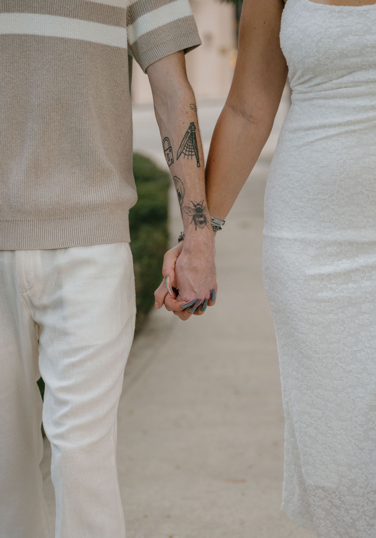 Close-up of a tattooed couple holding hands while walking together, showcasing their arm tattoos and bracelets.