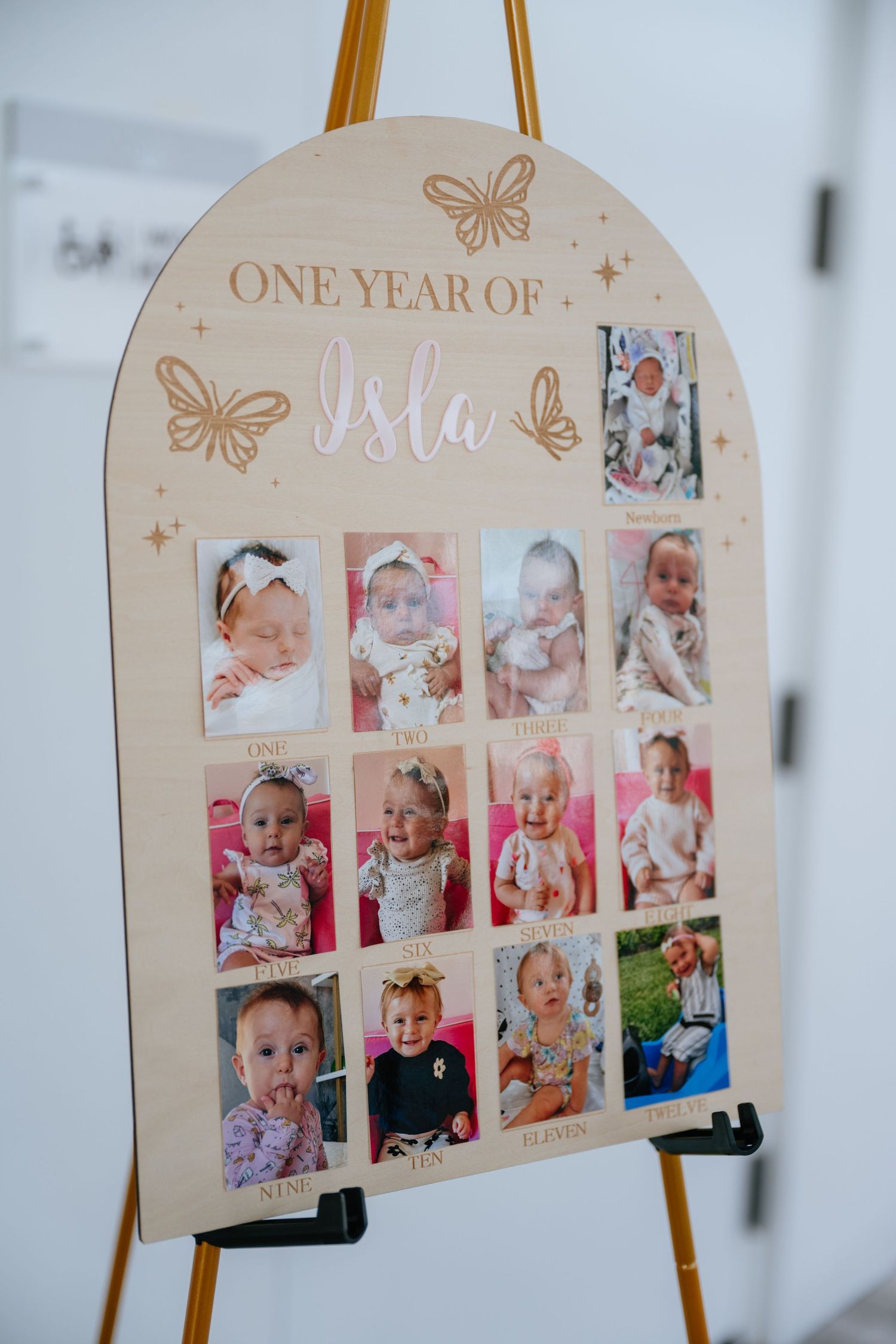 Wooden milestone photo board displaying one year of baby Isla's monthly growth photos with butterfly design.