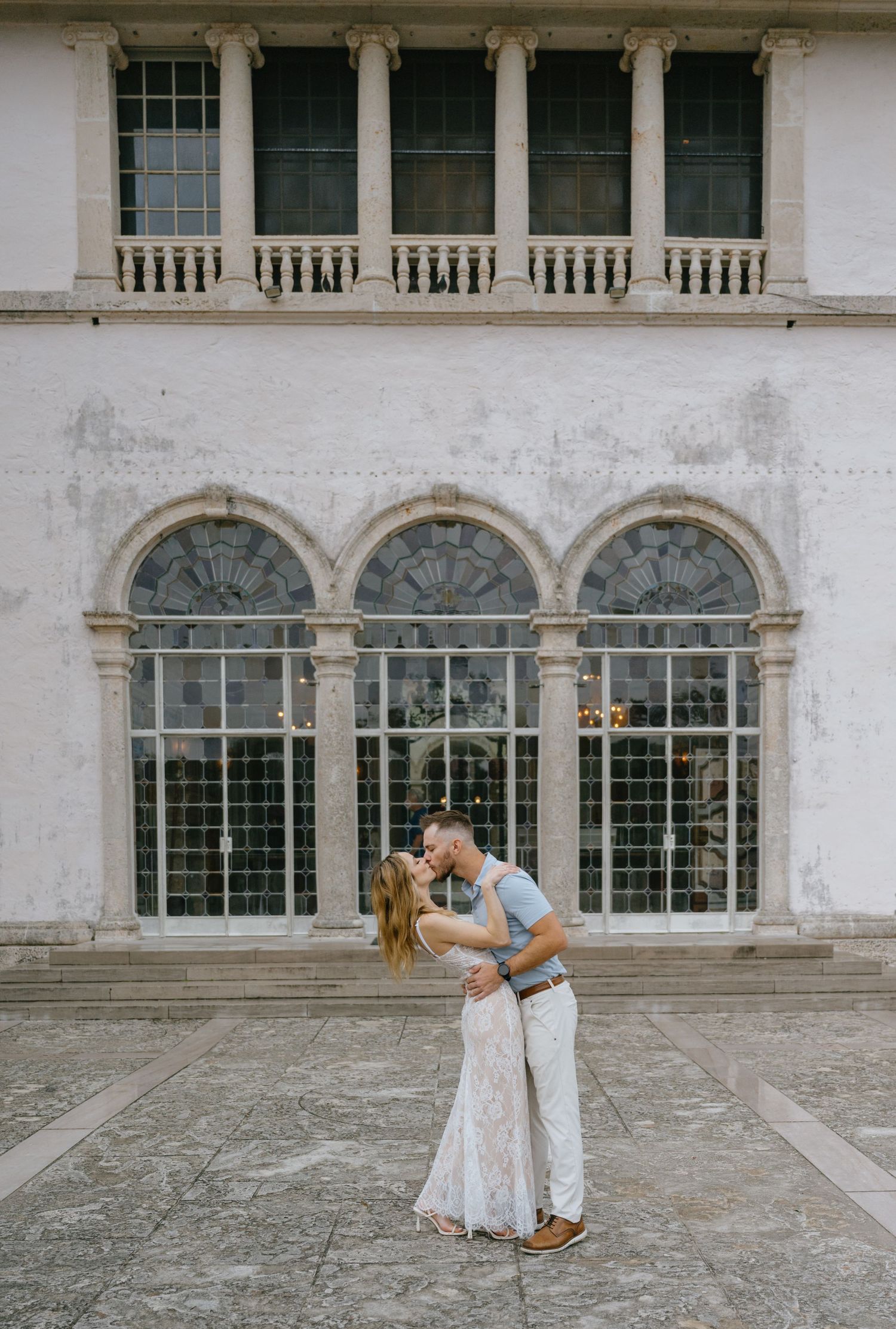 Couple sharing a romantic kiss in front of an elegant historic building facade.