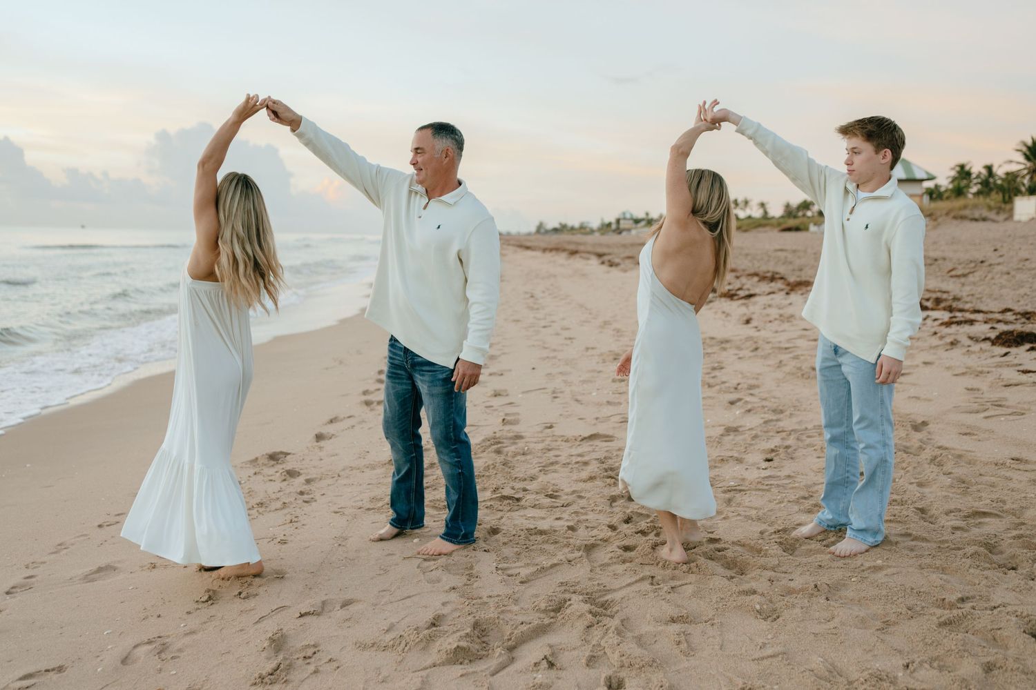 A family of four dances together on a sandy beach at sunset.