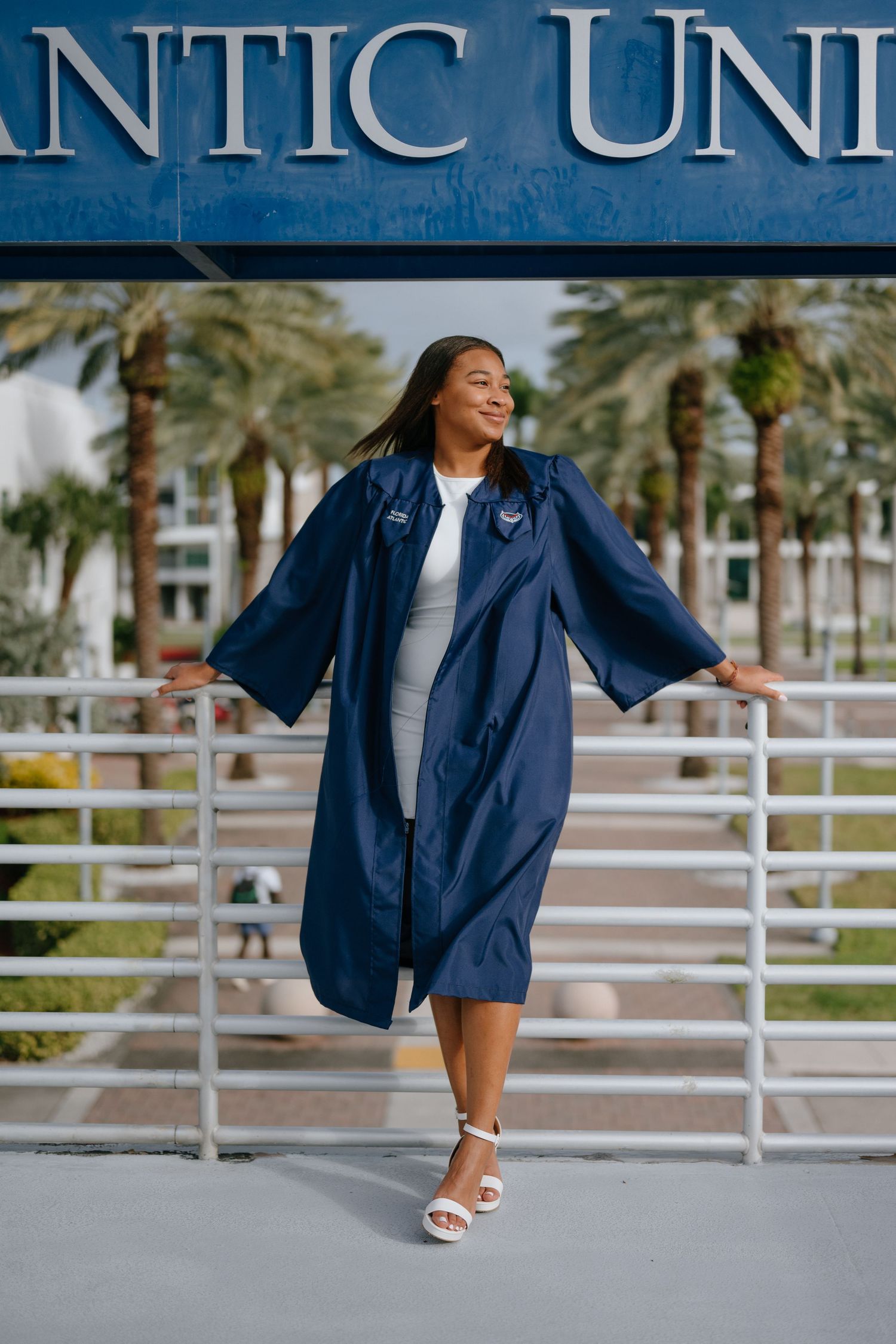 Graduate in navy gown posing confidently at Florida Atlantic University campus railing.