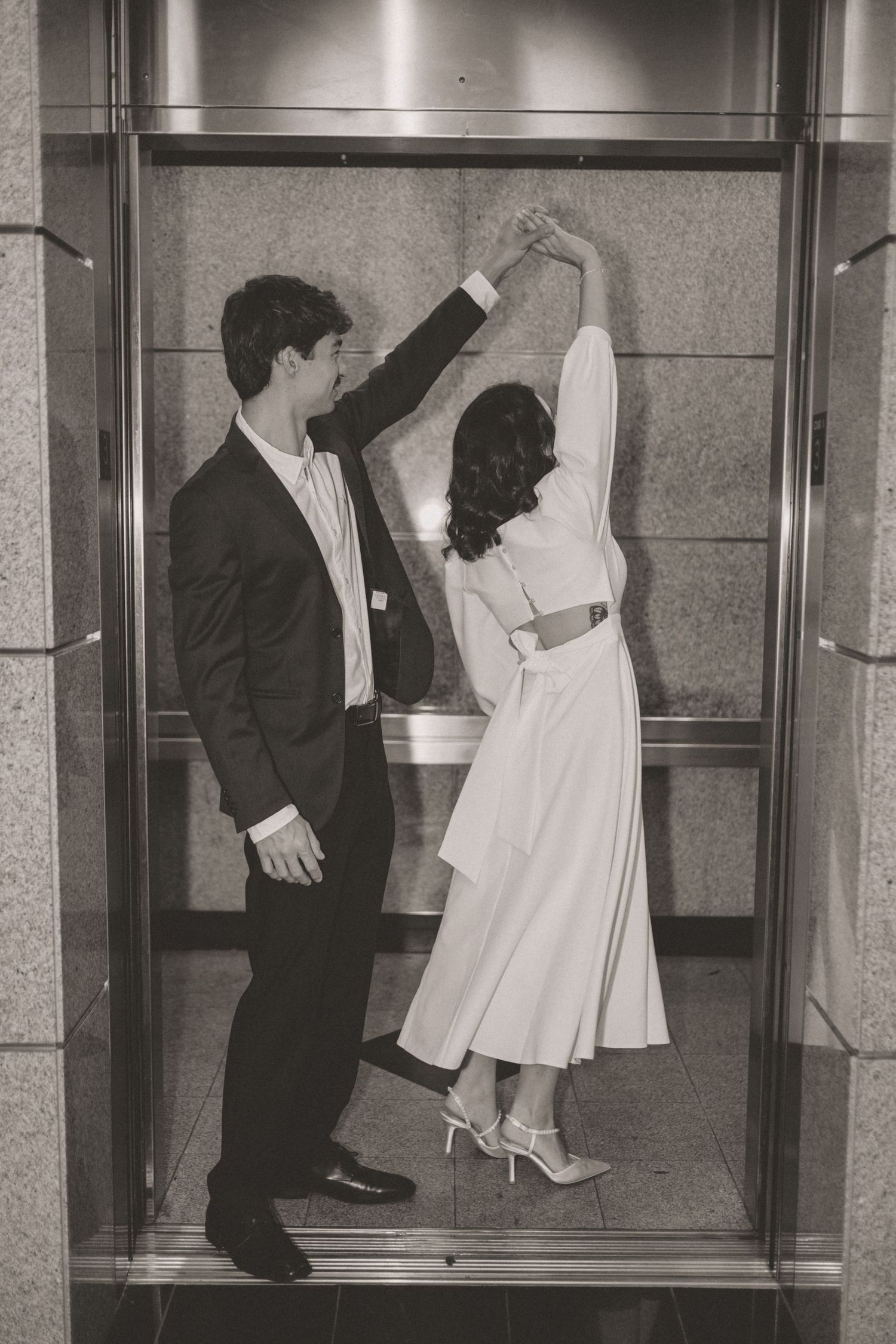 Black and white photo of bride and groom dancing together in elevator on their wedding day.