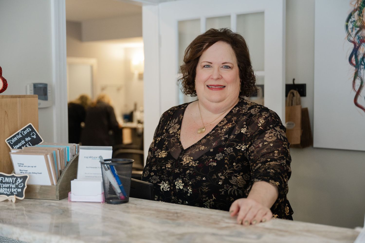 Friendly woman smiling behind reception desk in bright modern hair salon interior.